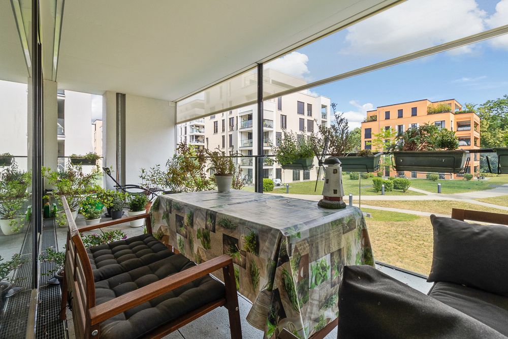 Überdachter Balkon mit Tisch, Stühlen und vielen Pflanzen, Blick auf moderne Wohngebäude.