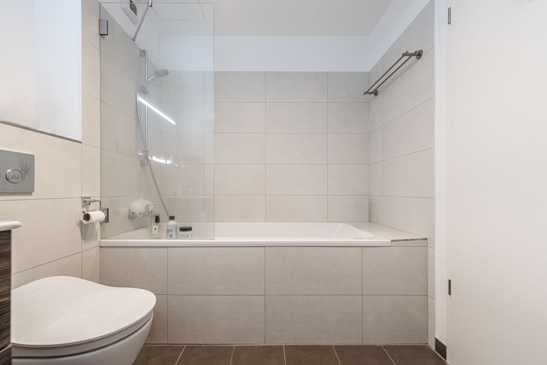 Modernes Badezimmer mit Badewanne, Glasduschwand, Toilettenpapierhalter und Wand-WC.