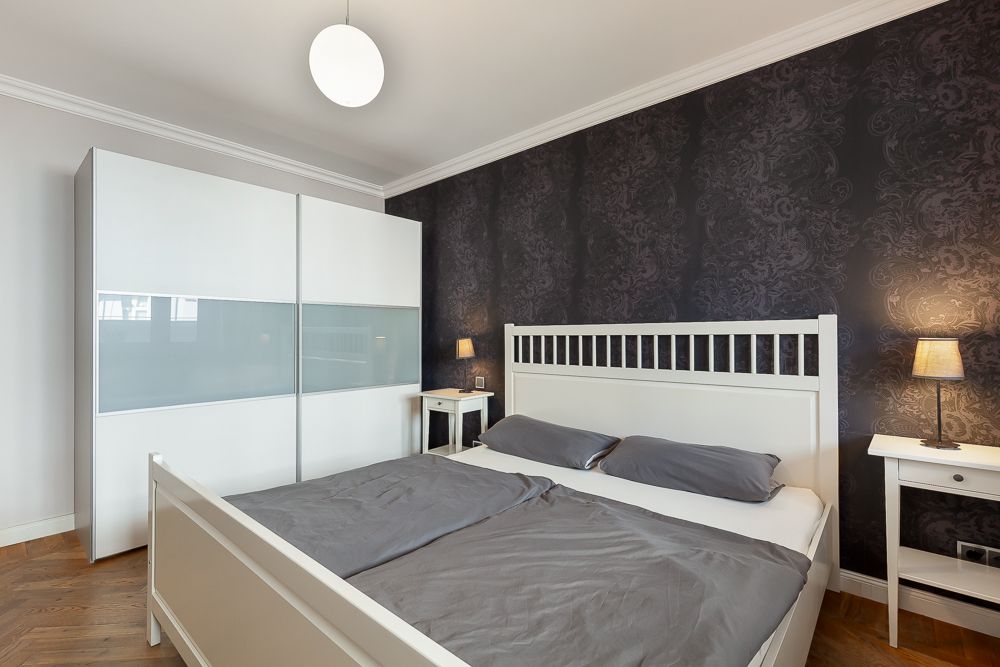 Schlafzimmer mit großem Bett, weißem Kleiderschrank und dunkler gemusterter Wand.