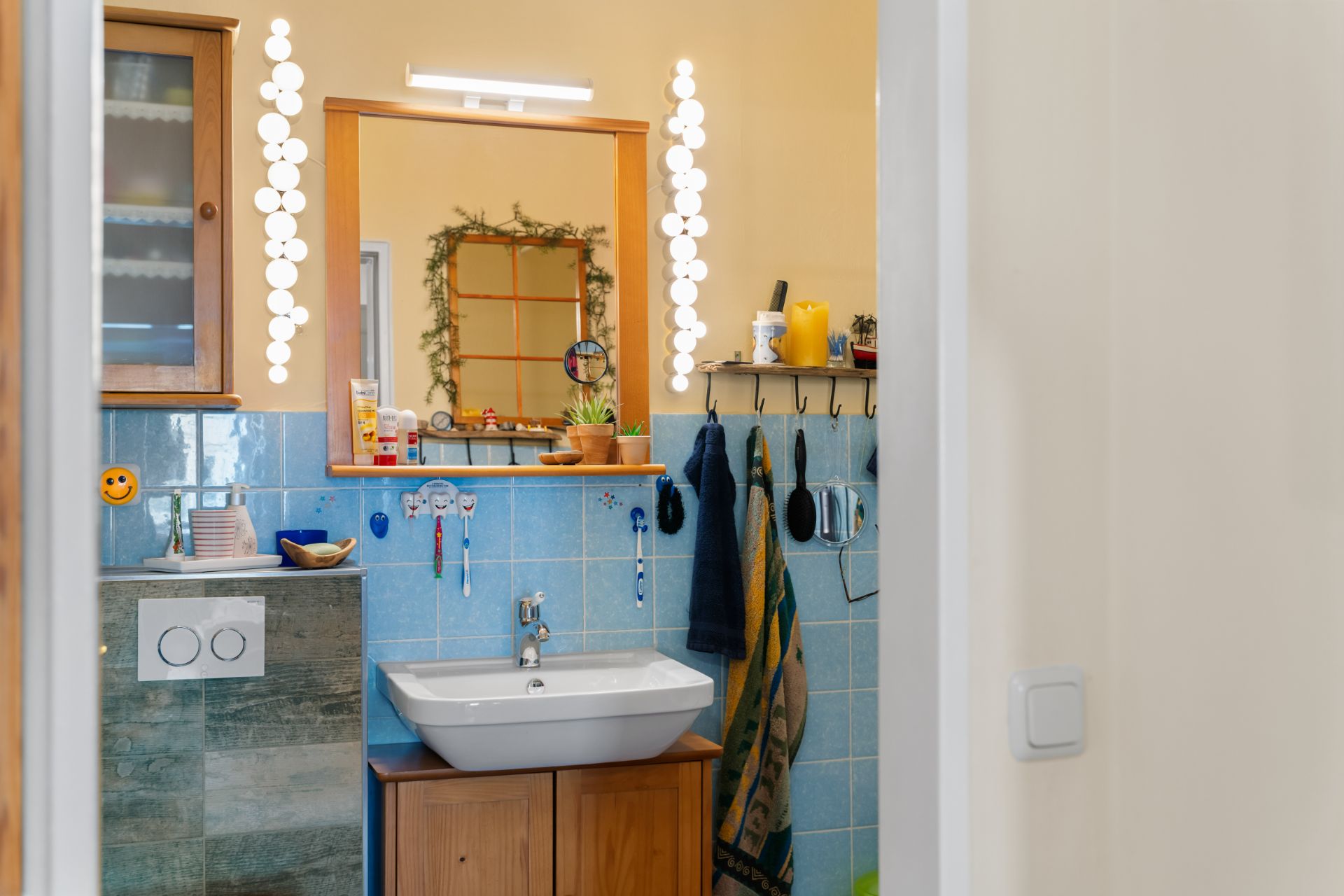 Badezimmer mit Waschbecken, Spiegel, blauen Fliesen und Handtüchern an Haken.