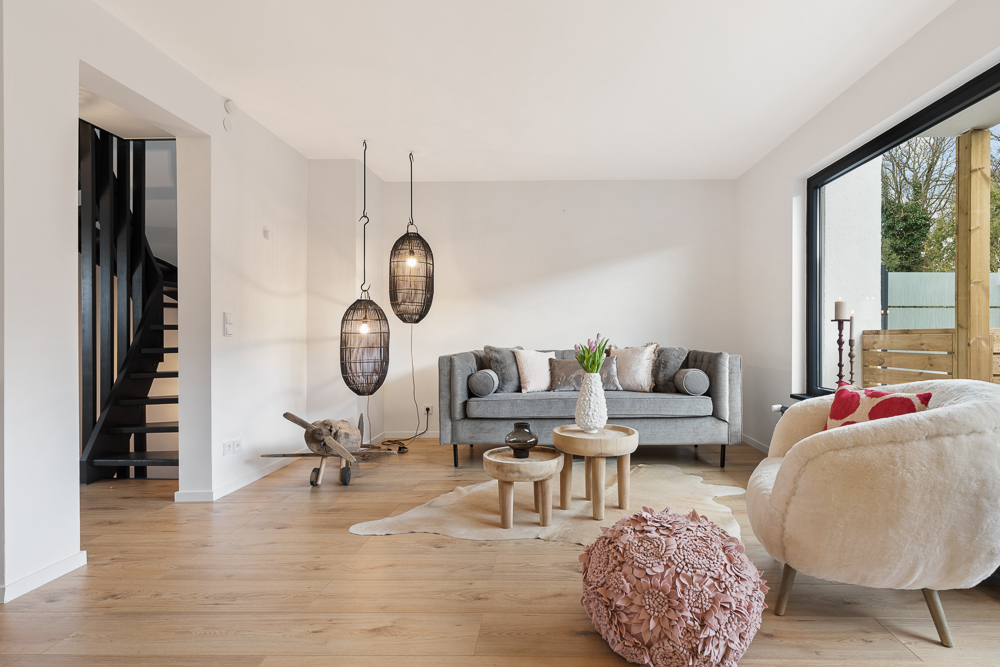 Modernes Wohnzimmer mit grauem Sofa, runden Tischen, Sessel und großen Fenstern.