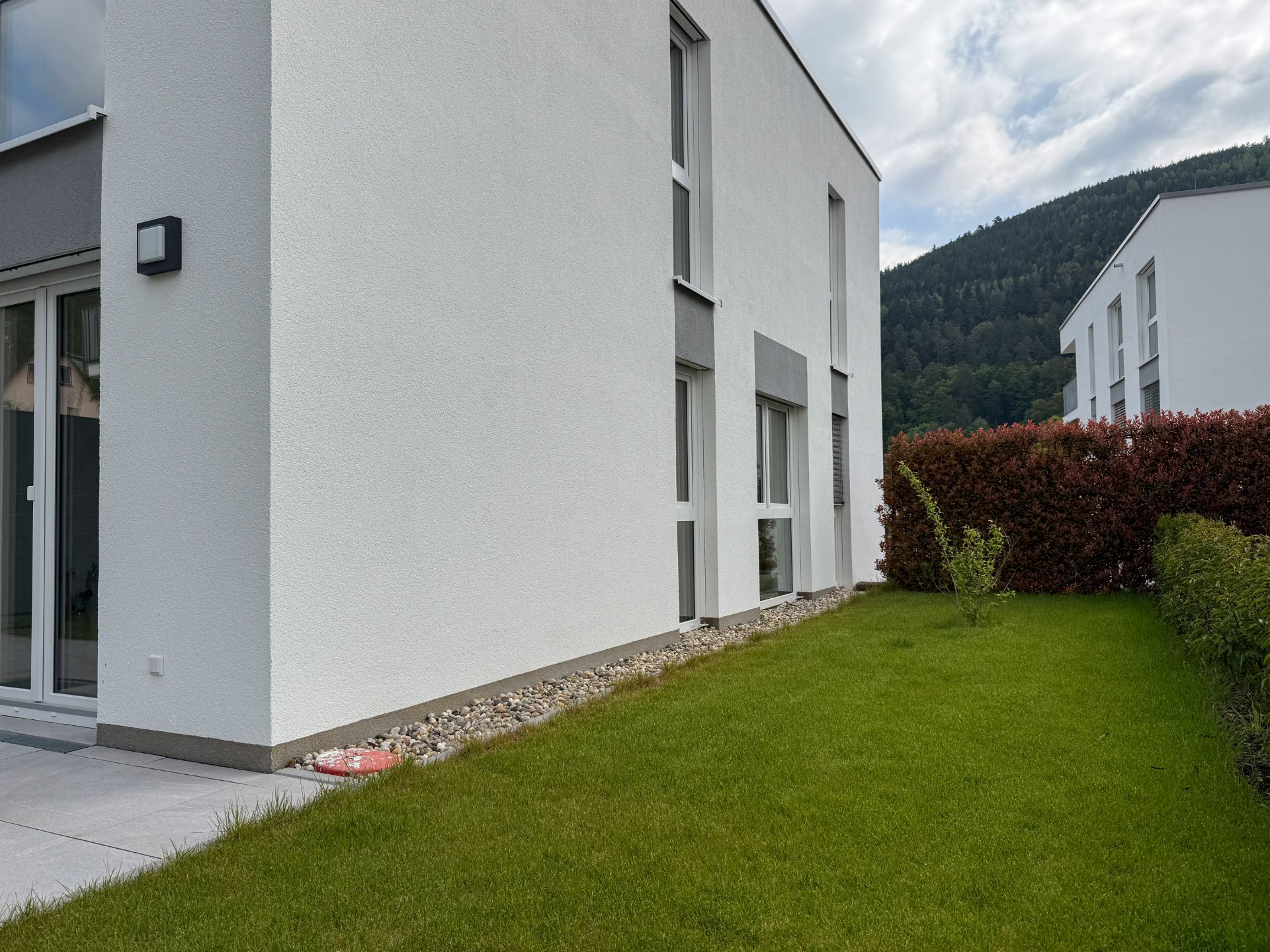 Moderne weiße Wohnhausfassade mit großen Fenstern und gepflegtem Garten.