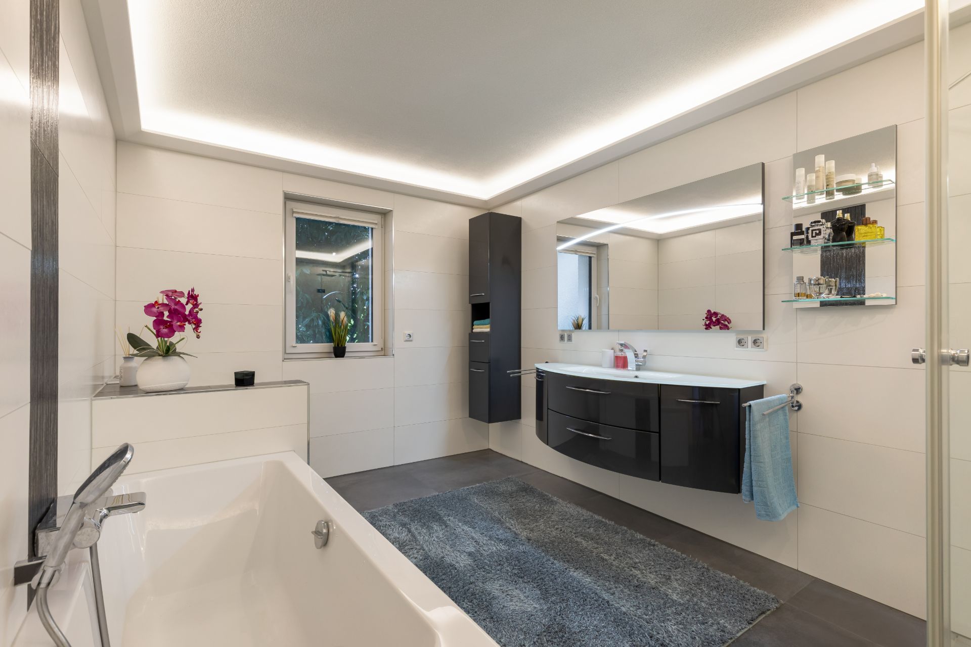 Modernes Badezimmer mit Badewanne, großem Spiegel, Waschbecken, Schrank und Fenster.
