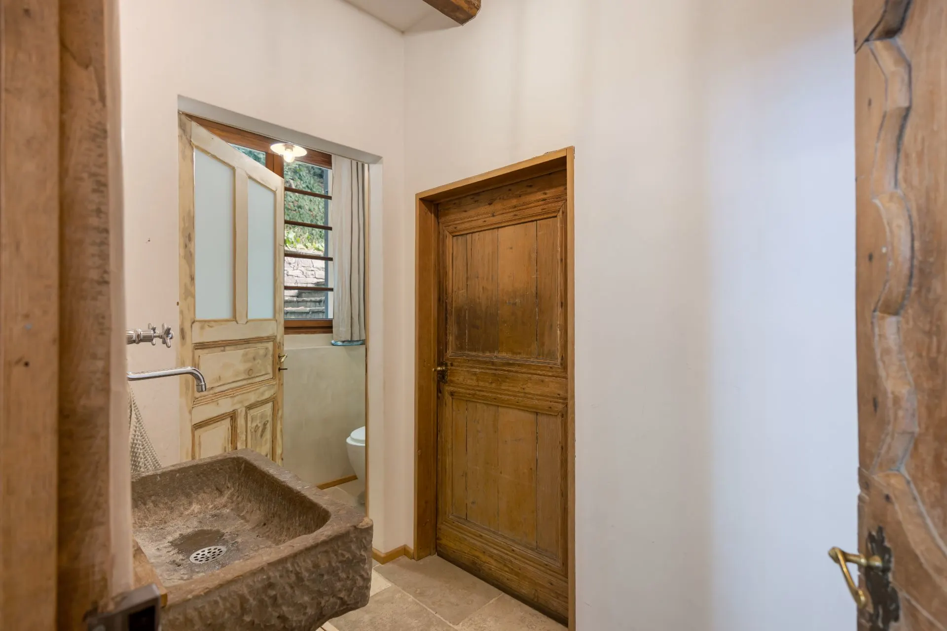 Kleines Badezimmer mit steinernem Waschbecken, Holztüren und Fenster.