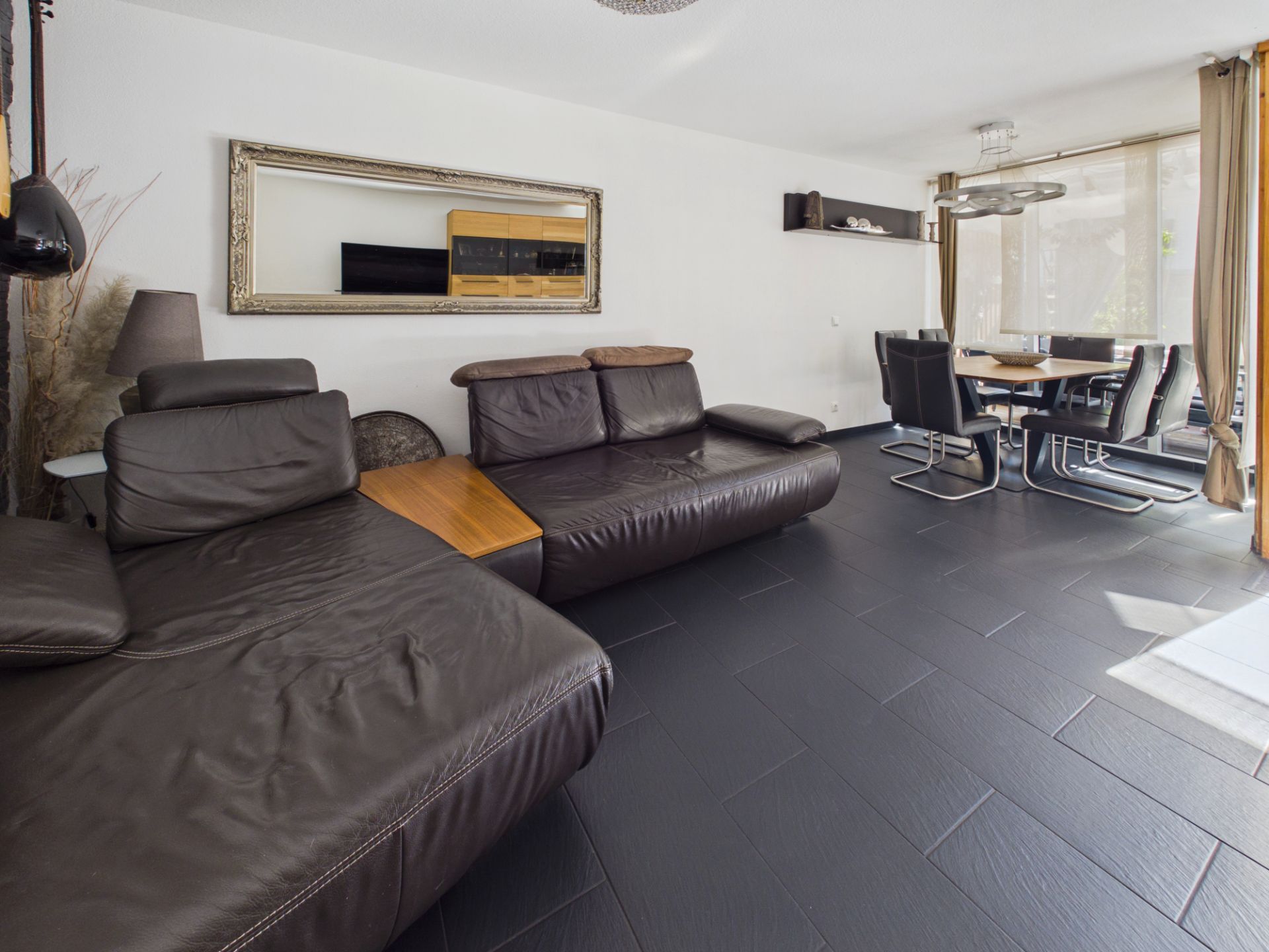 Modernes Wohnzimmer mit dunklem Ledersofa und Essbereich mit sechs Stühlen am Fenster.