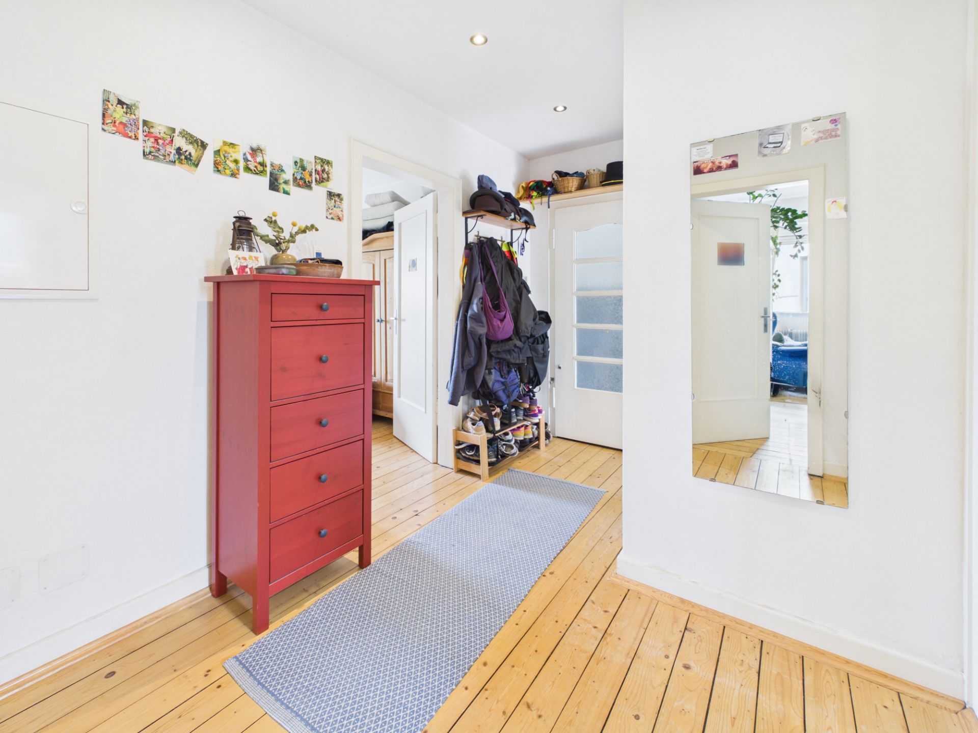 Heller Flur mit roter Kommode, großem Spiegel und Garderobe auf Holzboden.