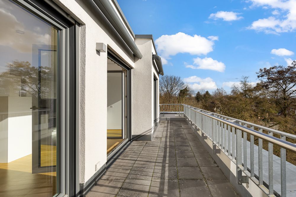 Geräumiger Balkon an einem Wohnhaus mit Glastüren und Blick ins Grüne.