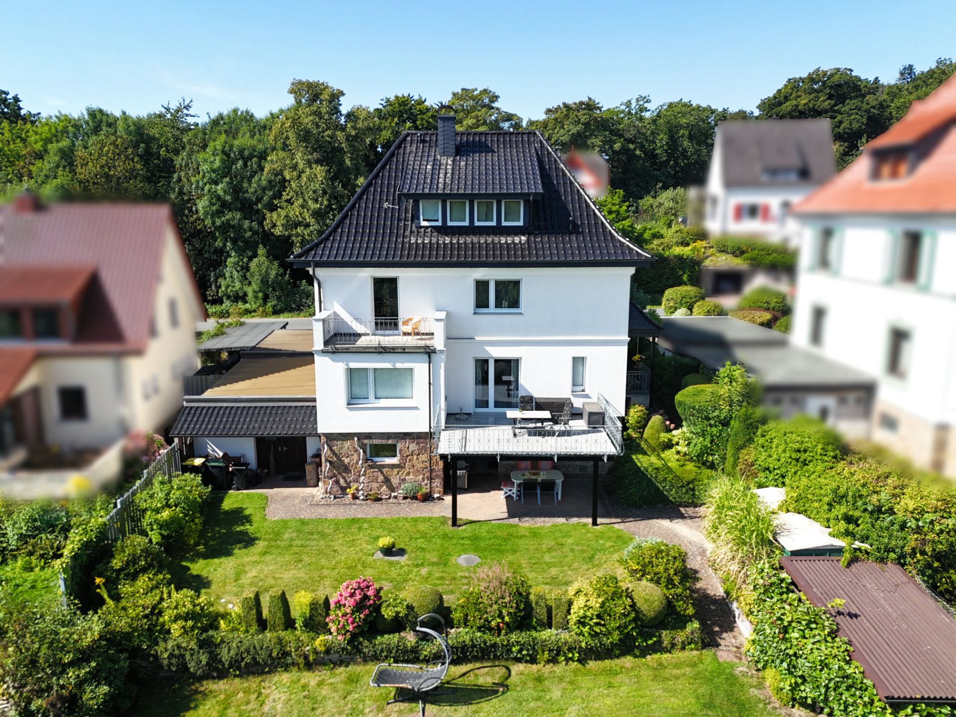 Zweistöckiges Wohnhaus mit Balkon, Terrasse und gepflegtem Garten im Vordergrund.