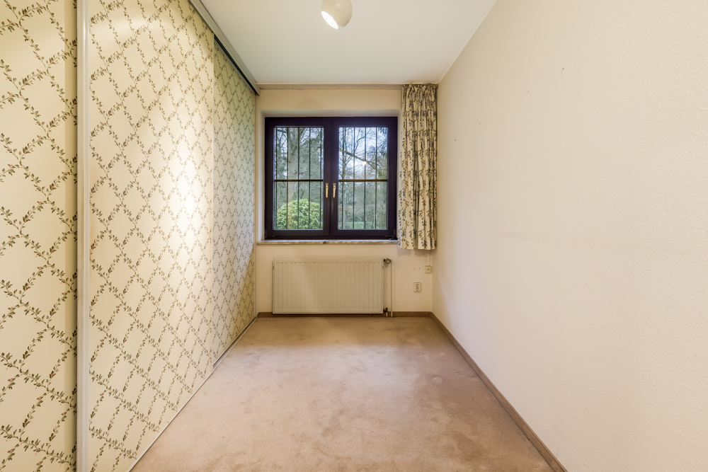 Kleines Zimmer mit Teppichboden, Fenster mit Vorhang und gemusterter Schiebetür.