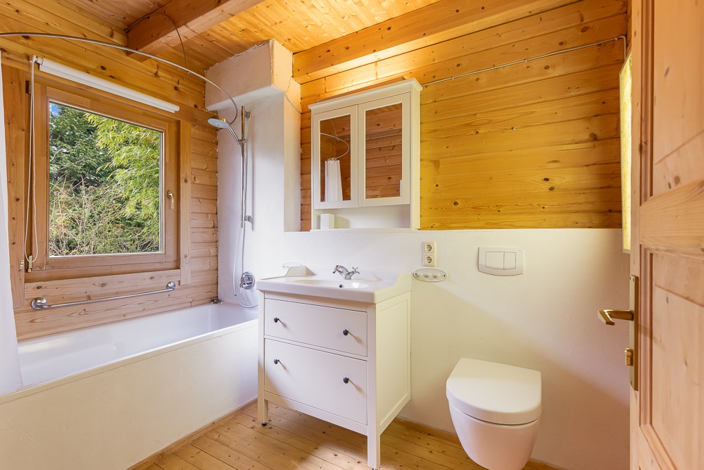 Helles Badezimmer mit Holzverkleidung, Badewanne, Waschbecken, Spiegel und Toilette.