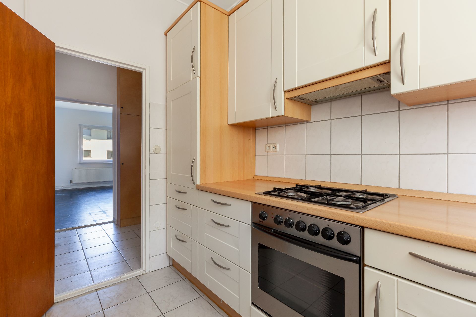 Helle Einbauküche mit Gasherd, Backofen und weißen Fliesen, Blick ins angrenzende Zimmer.