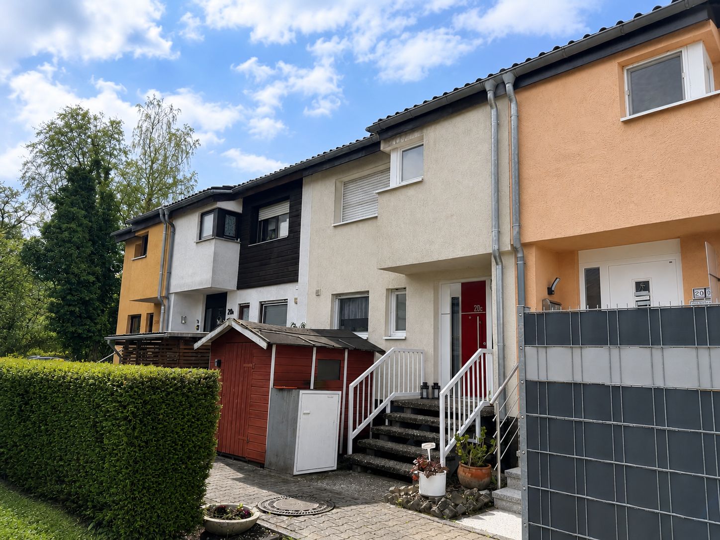 Reihenhaus mit kleinem Schuppen, Stufen zum Eingang und Hecke im Vordergrund.