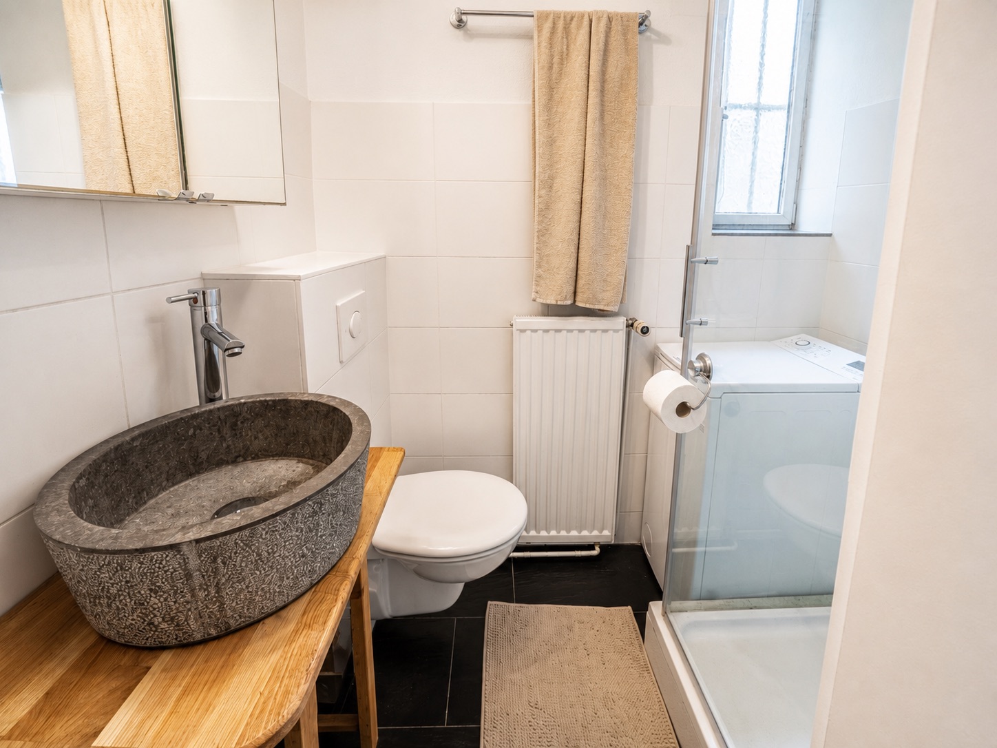 Modernes Badezimmer mit steinerner Waschschale, Dusche, Toilette und Handtuch an der Wand.