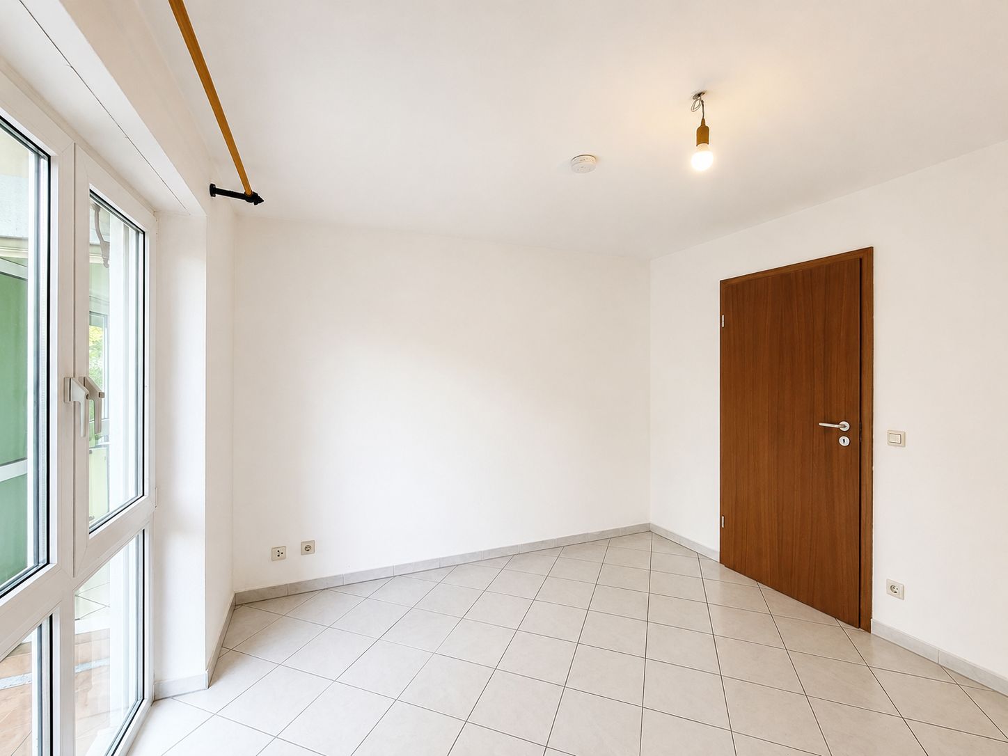 Heller leerer Raum mit weißen Wänden, Fliesenboden, Fenster und Holztür.