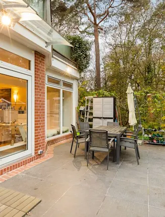 Große Terrasse mit Esstisch, Stühlen, Gartenhaus und Blick ins Wohnzimmer durch große Fenster.