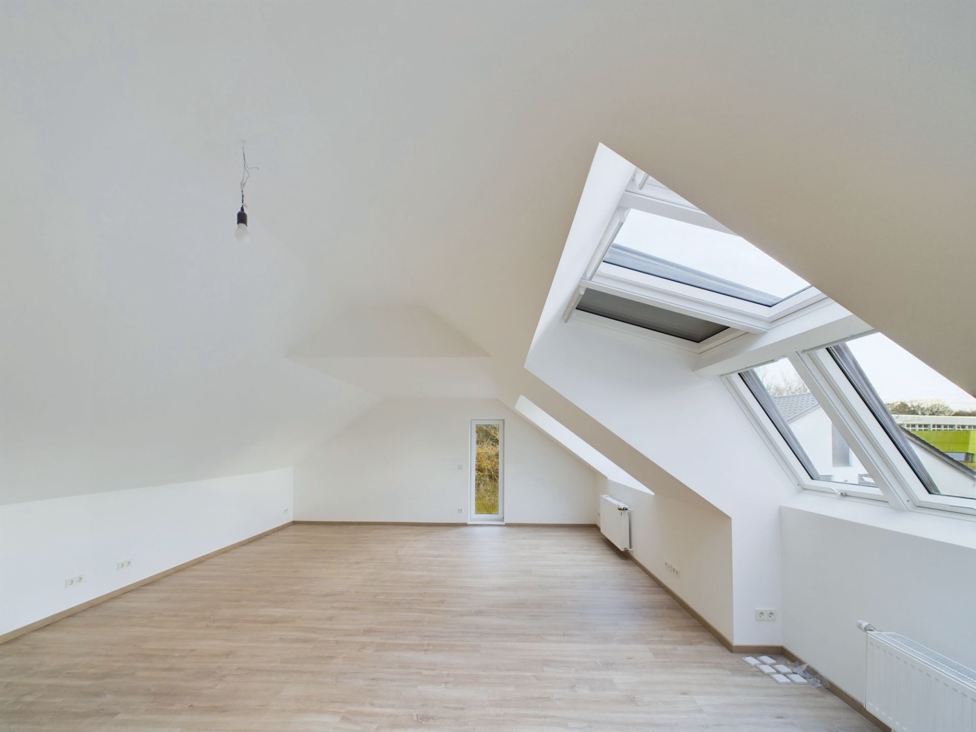 Heller Dachgeschossraum mit schrägen Wänden, großen Fenstern und Laminatboden.