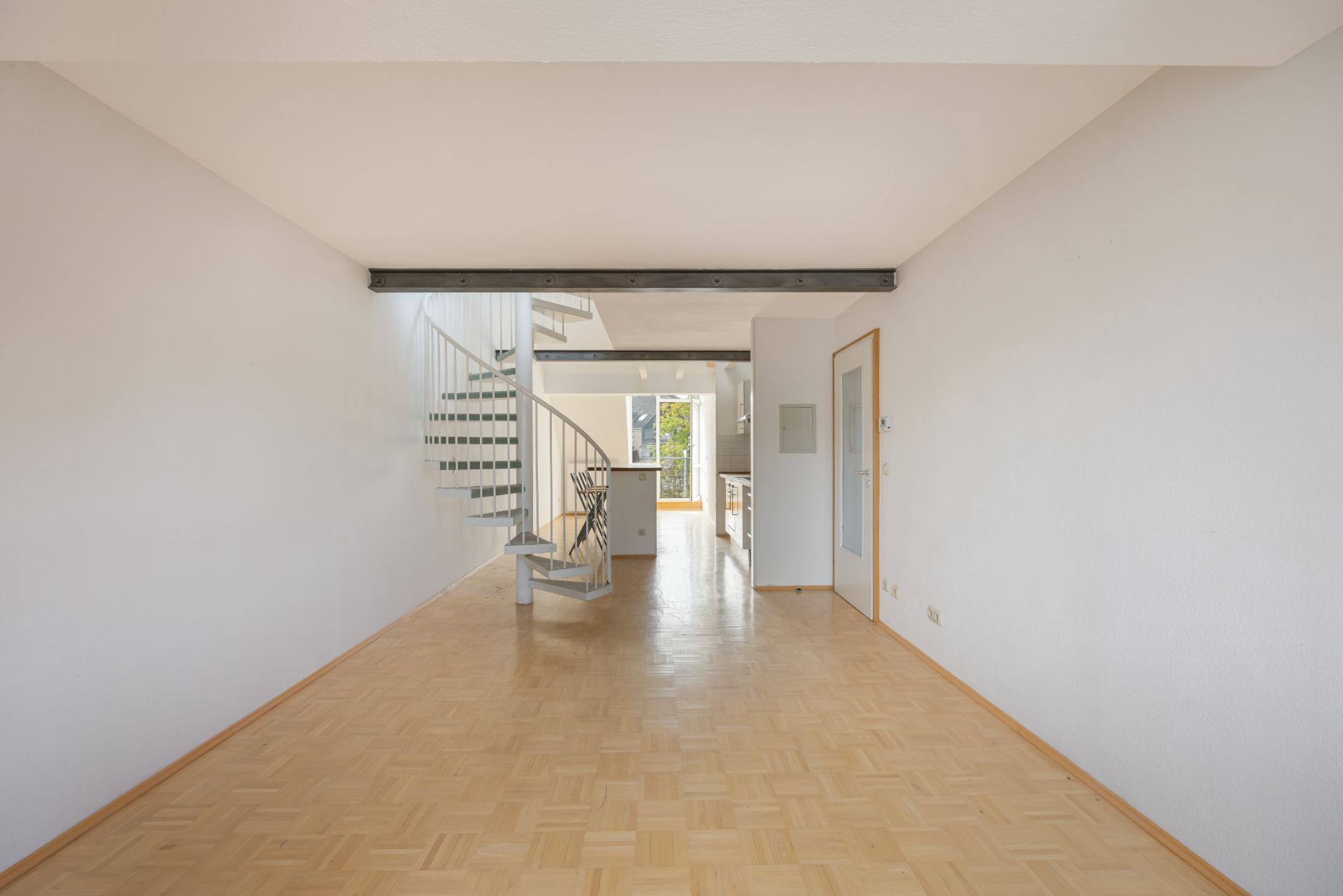 Heller Raum mit Holzfußboden und offener Wendeltreppe, führt zur Küche.