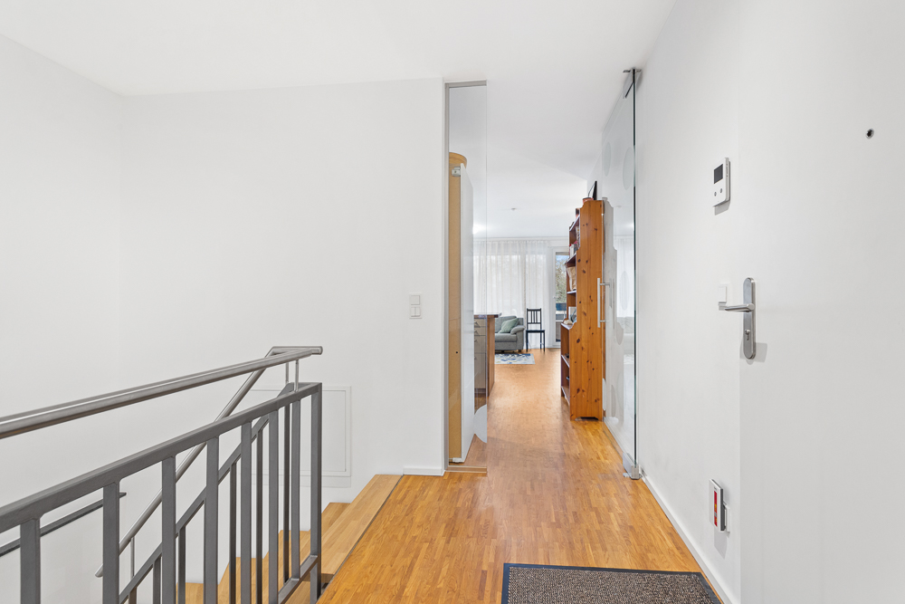 Heller Flur mit Holzboden, Treppe und Blick ins Wohnzimmer mit Regal.