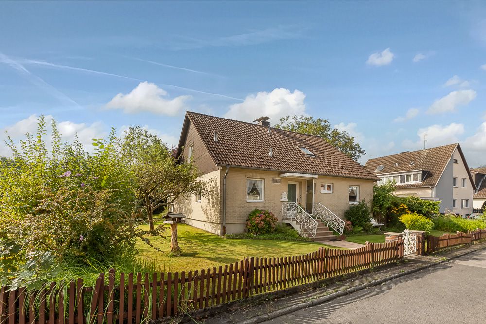 Einfamilienhaus mit Garten, braunem Zaun und gepflegtem Vorgarten an einer ruhigen Straße.