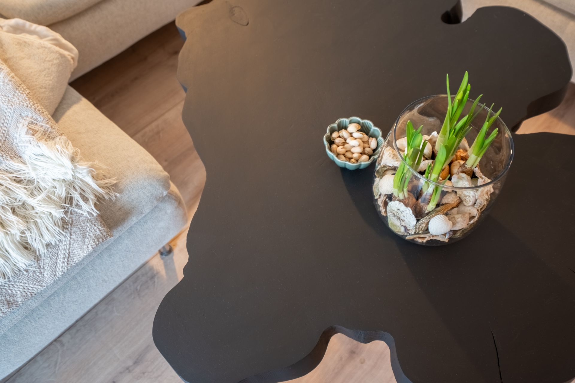 Schwarzer Couchtisch mit Pflanzenglas und kleiner Schale mit Nüssen, daneben ein beiger Sessel mit Decke.