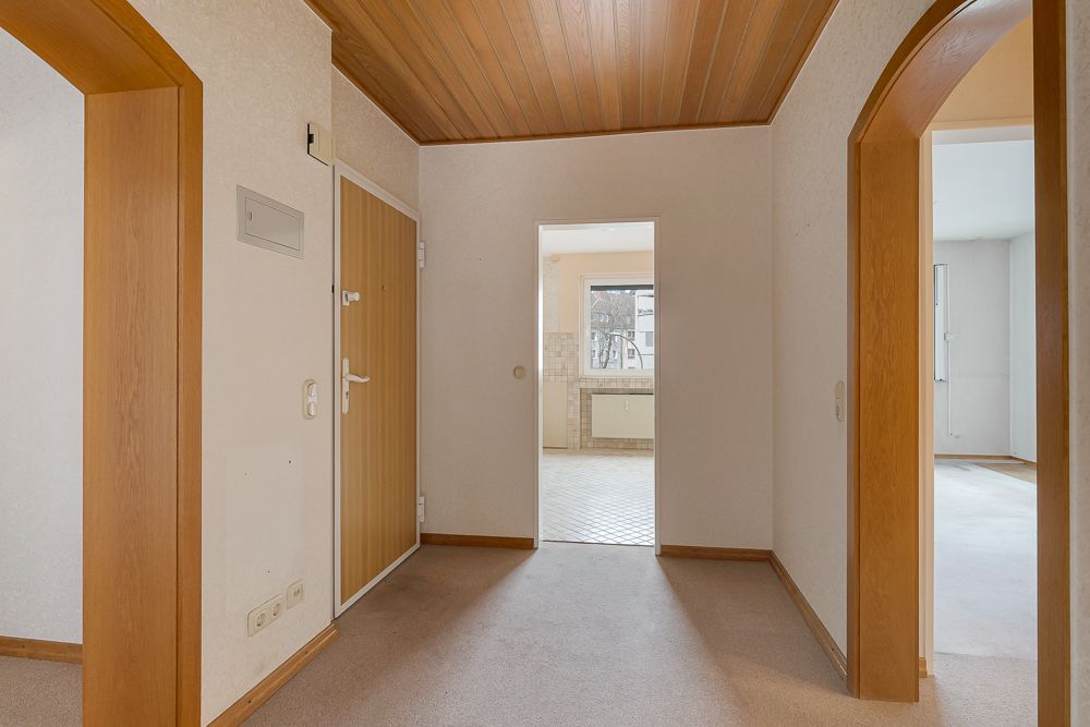 Flur mit Holztür, Holzbogen und Blick in eine Küche mit Fenster.