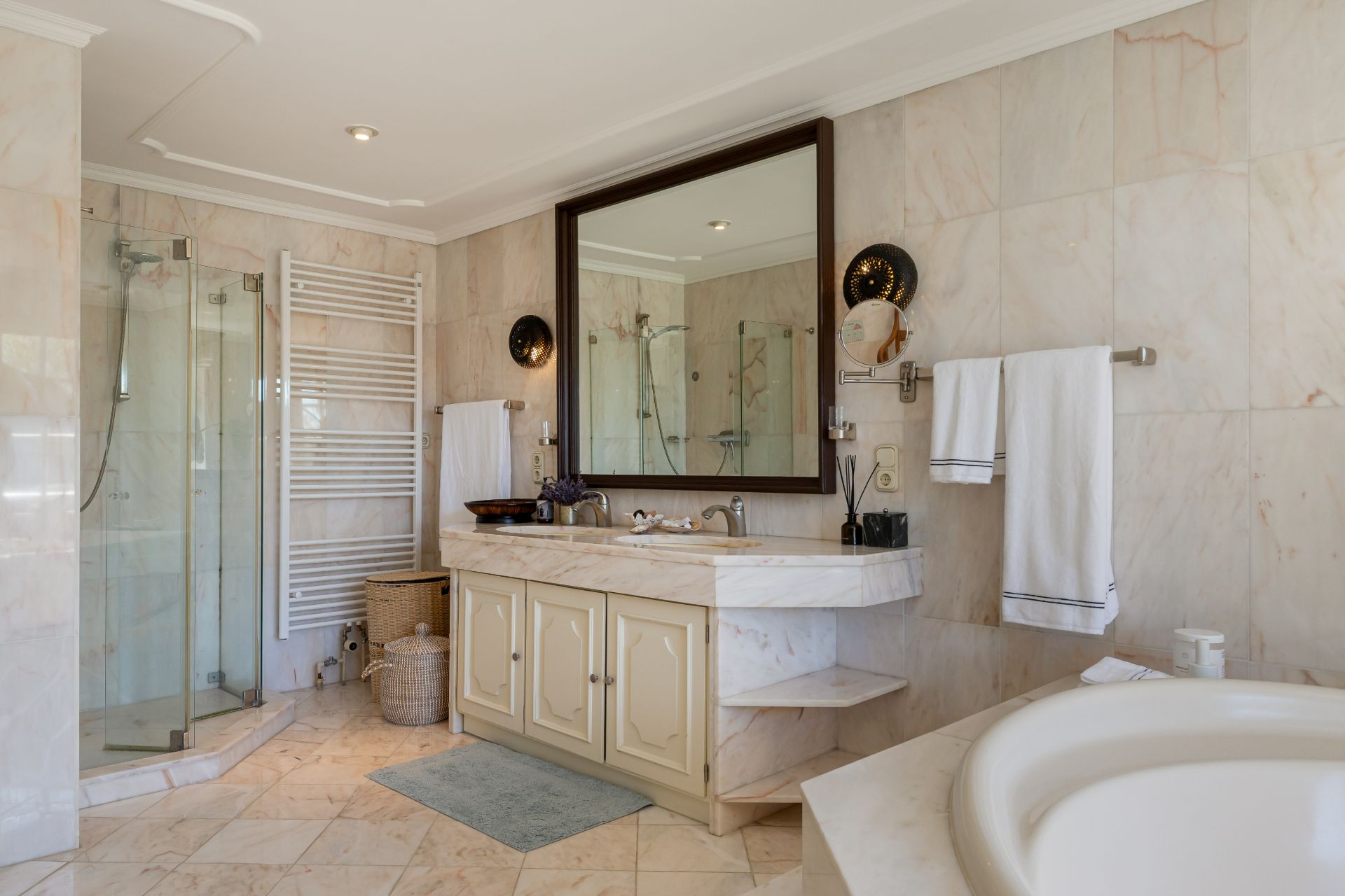 Helles Badezimmer mit großer Dusche, Doppelwaschbecken, Spiegel, Handtuchhaltern und Badewanne.