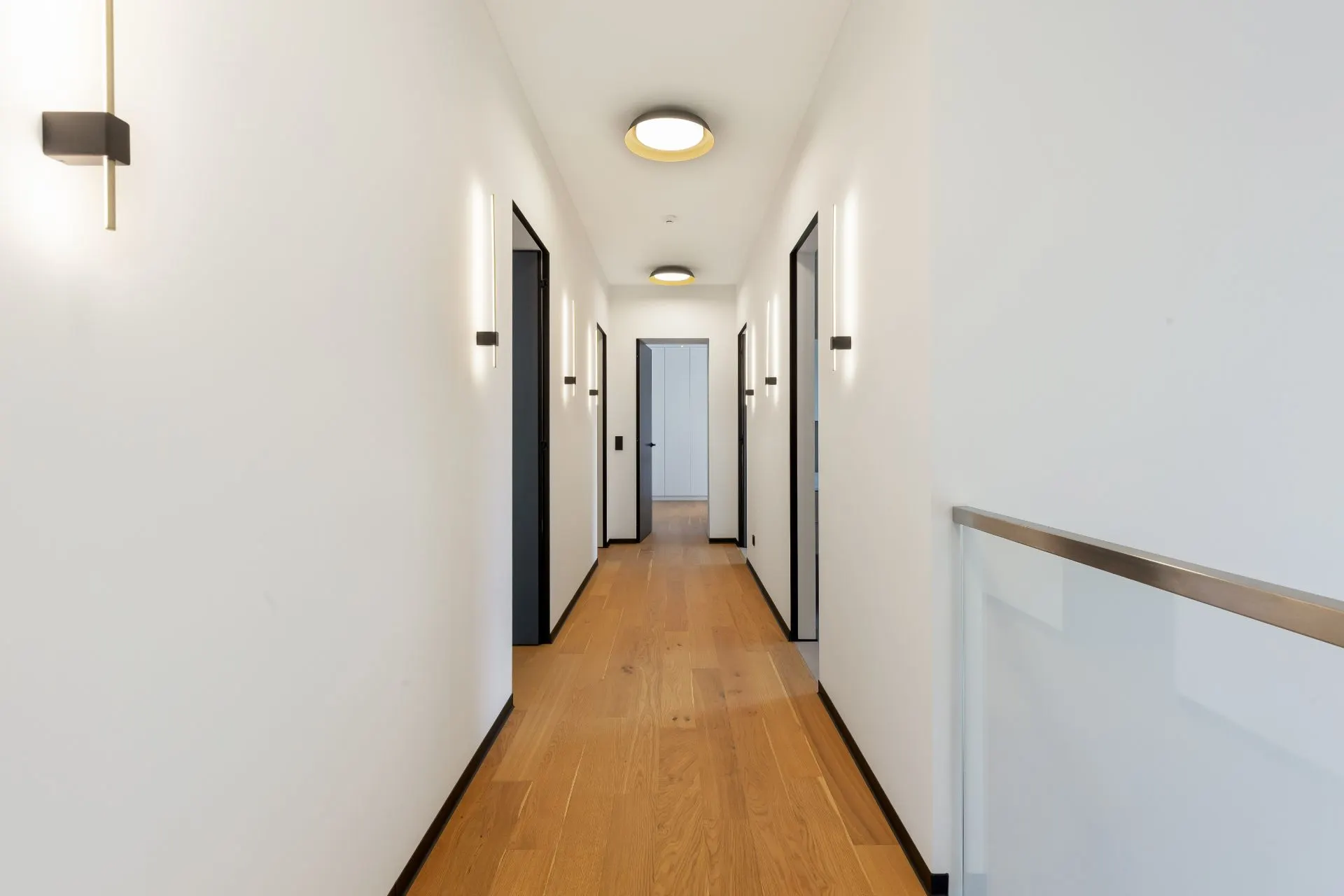 Heller Flur mit Holzfußboden, weißen Wänden und mehreren Türen zu beiden Seiten.