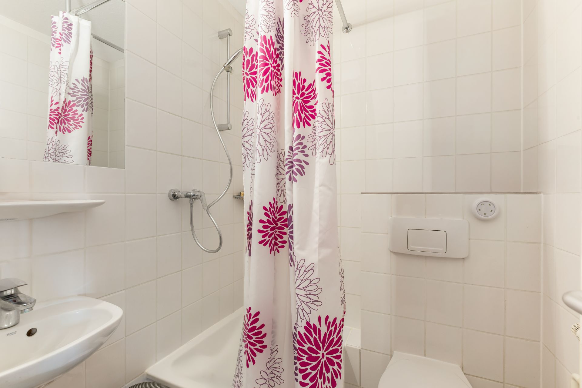 Kleines Badezimmer mit Duschvorhang, Waschbecken, Toilette und Dusche mit Handbrause.