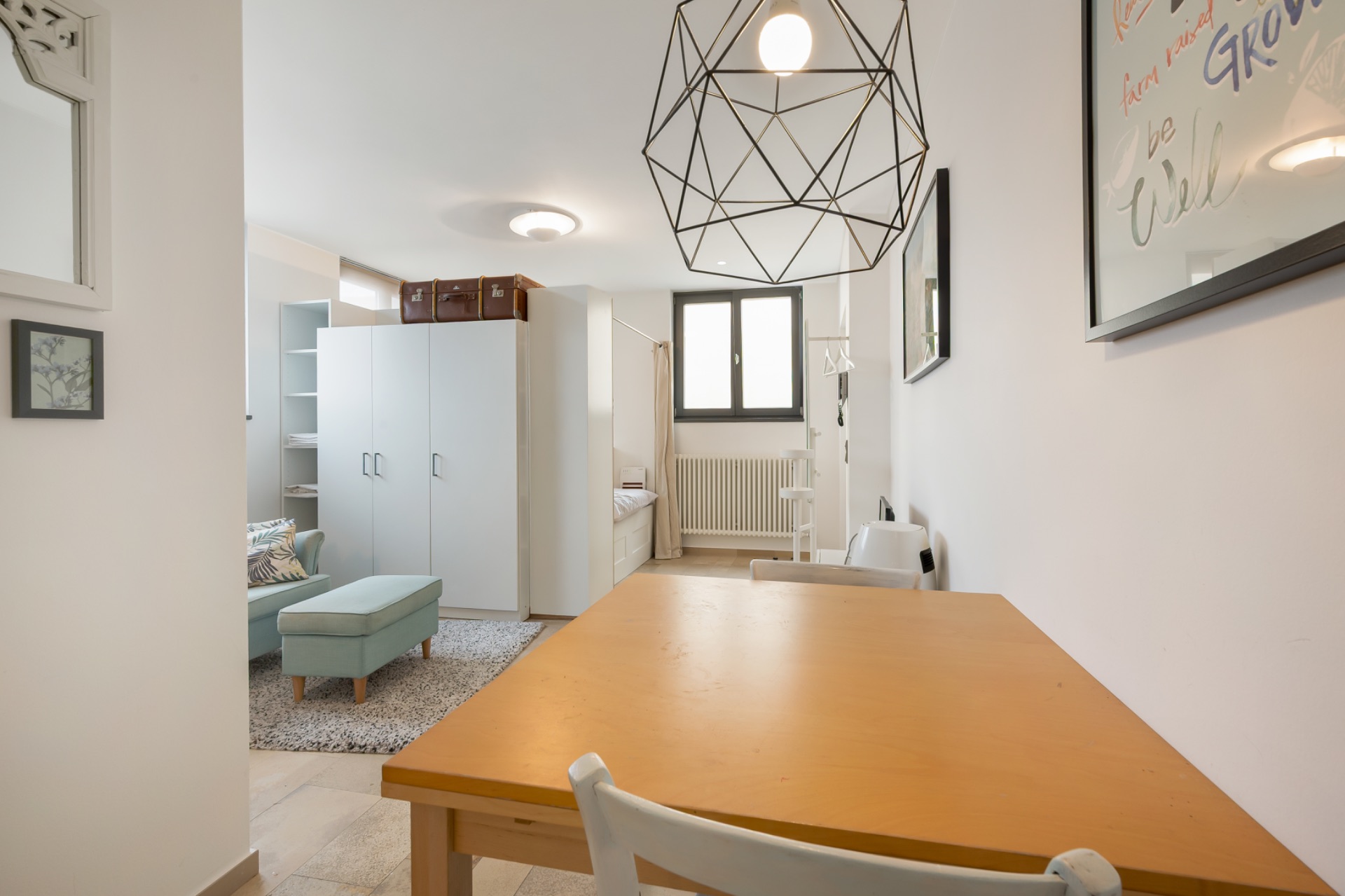 Helles Wohnzimmer mit Holztisch, Stuhl, Kleiderschrank, Ottomanen und Fenster.