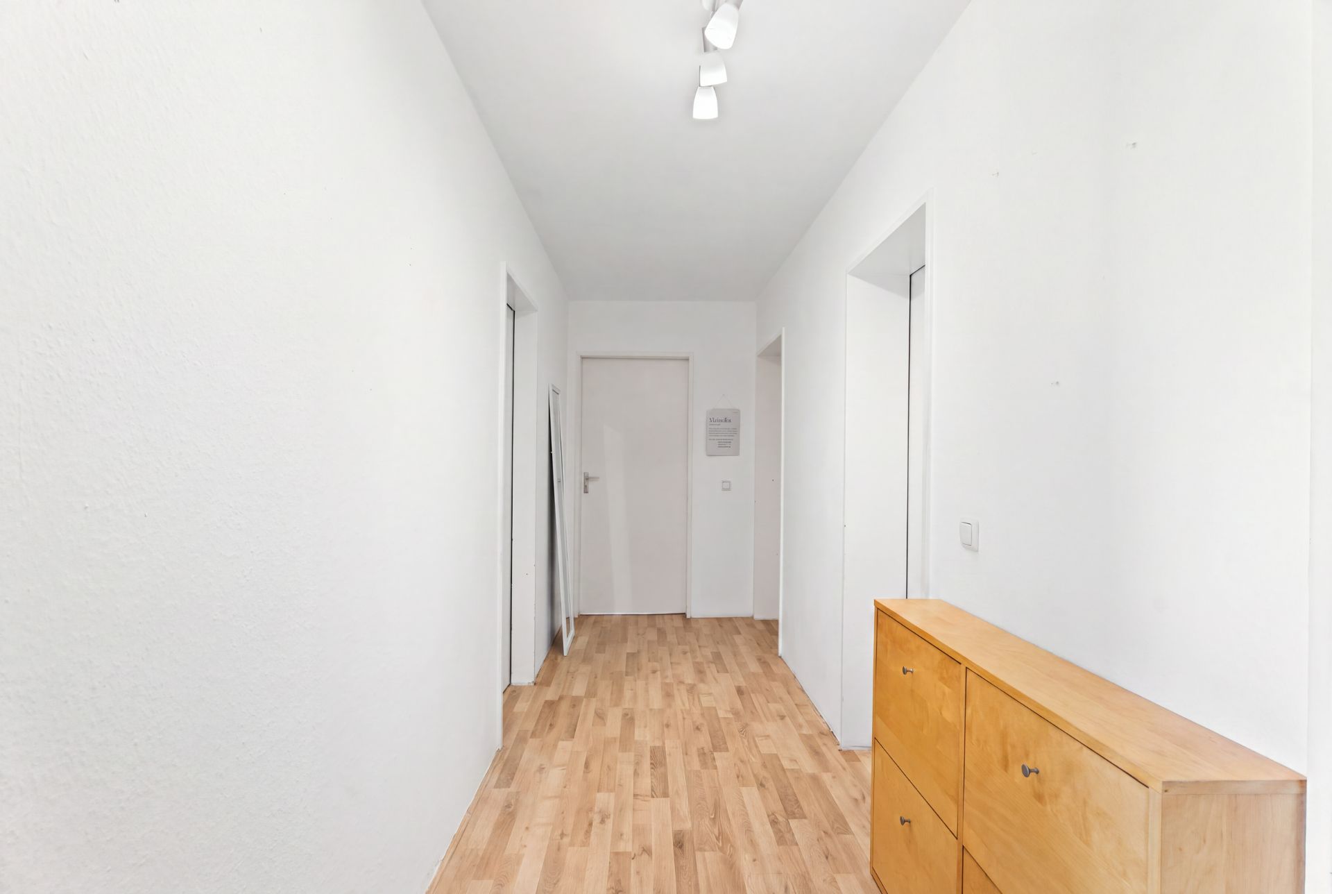 Heller Flur mit Holzfußboden, weißen Wänden und einer Holzkommode rechts.