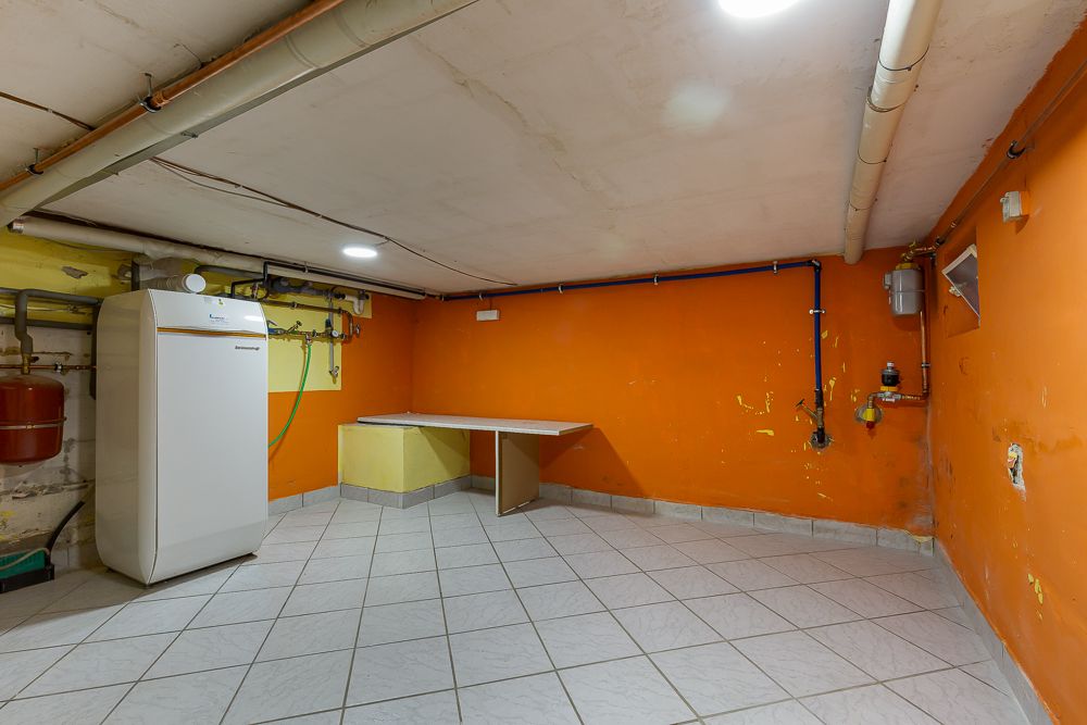 Kellerraum mit orangenen Wänden, Fliesenboden, Heizgerät und einem kleinen Tisch in der Ecke.