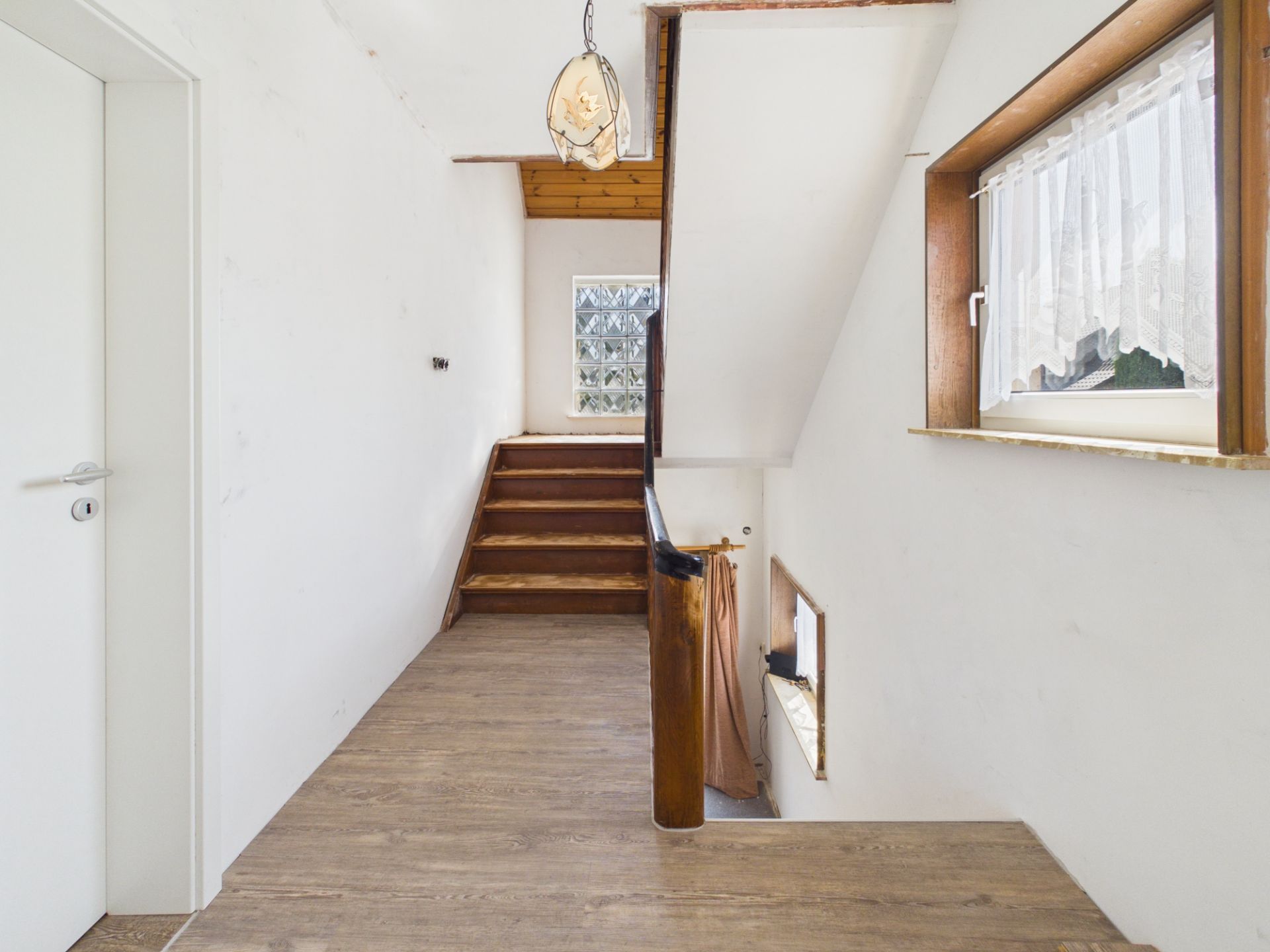 Heller Flur mit Holztreppe, Fenster und Hängelampe in einem Wohnhaus.
