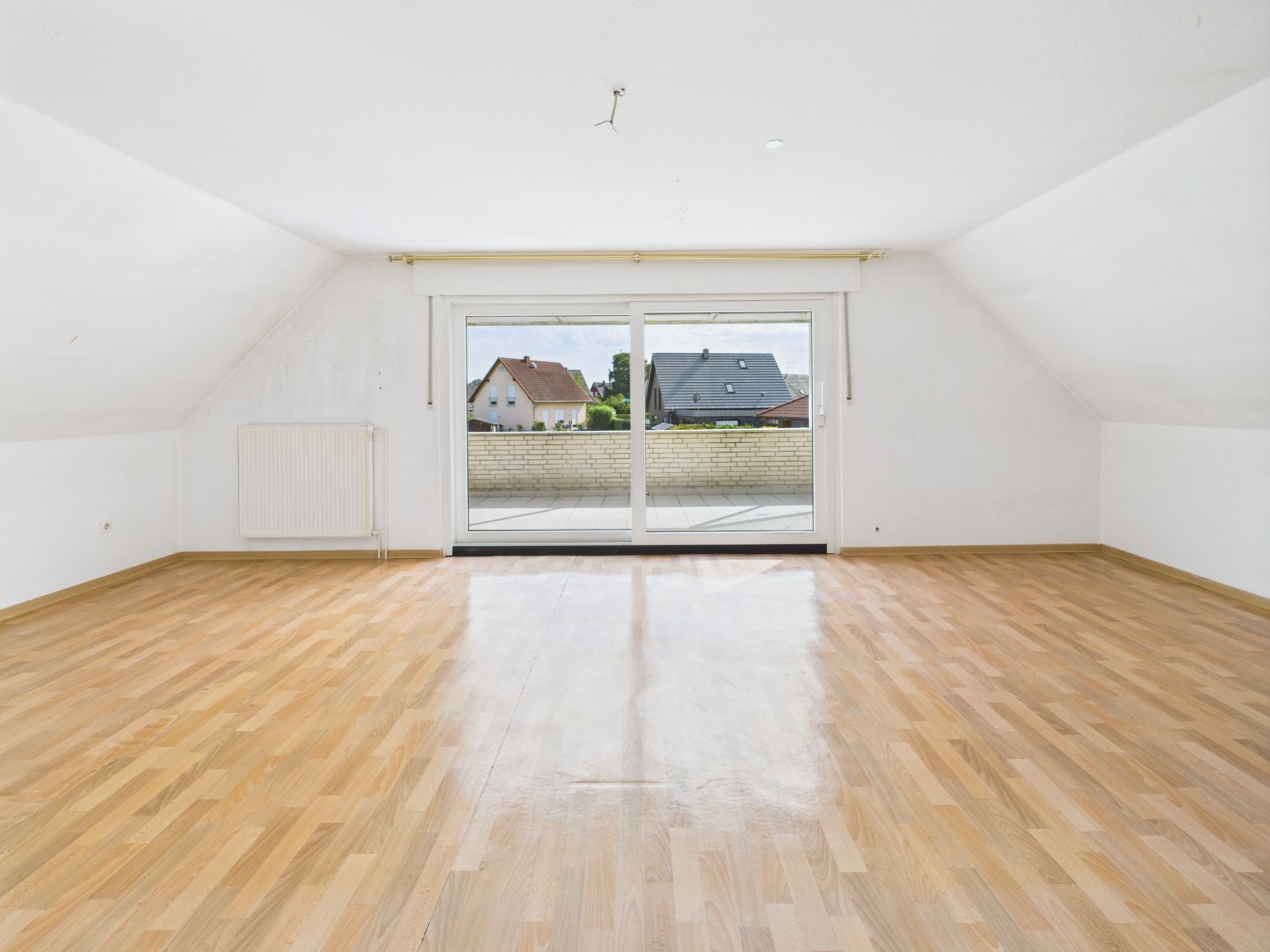 Leerer Raum mit hellem Holzfußboden und großer Glastür zu einem Balkon.