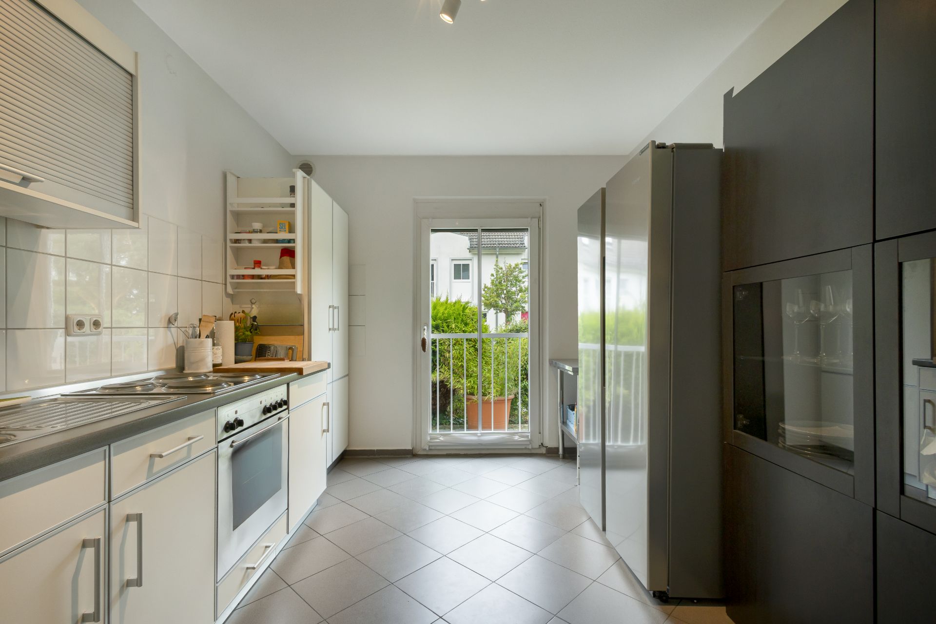 Moderne Küche mit weißen Schränken, großen Fenstern und Zugang zum Balkon.