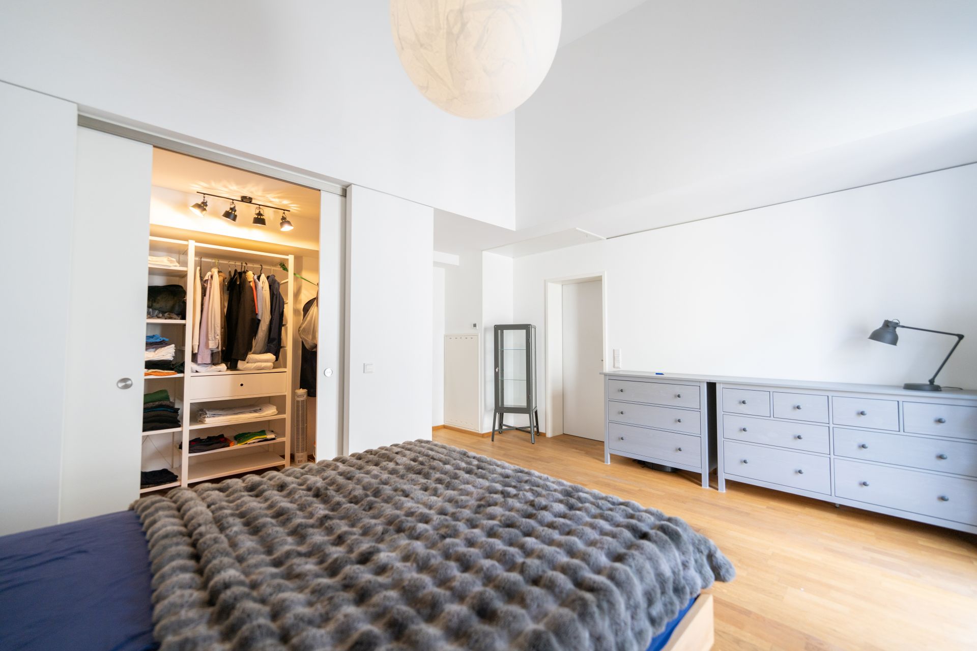 Helles Schlafzimmer mit Bett, Kleiderschrank, Kommoden und Holzfußboden.