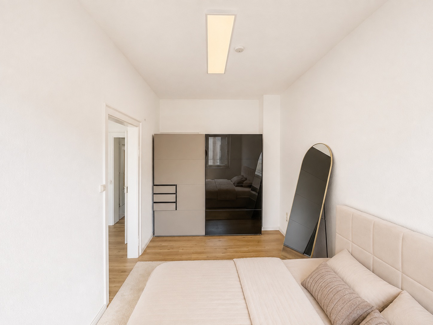 Schlafzimmer mit Bett, Kleiderschrank und großem Spiegel an der Wand.