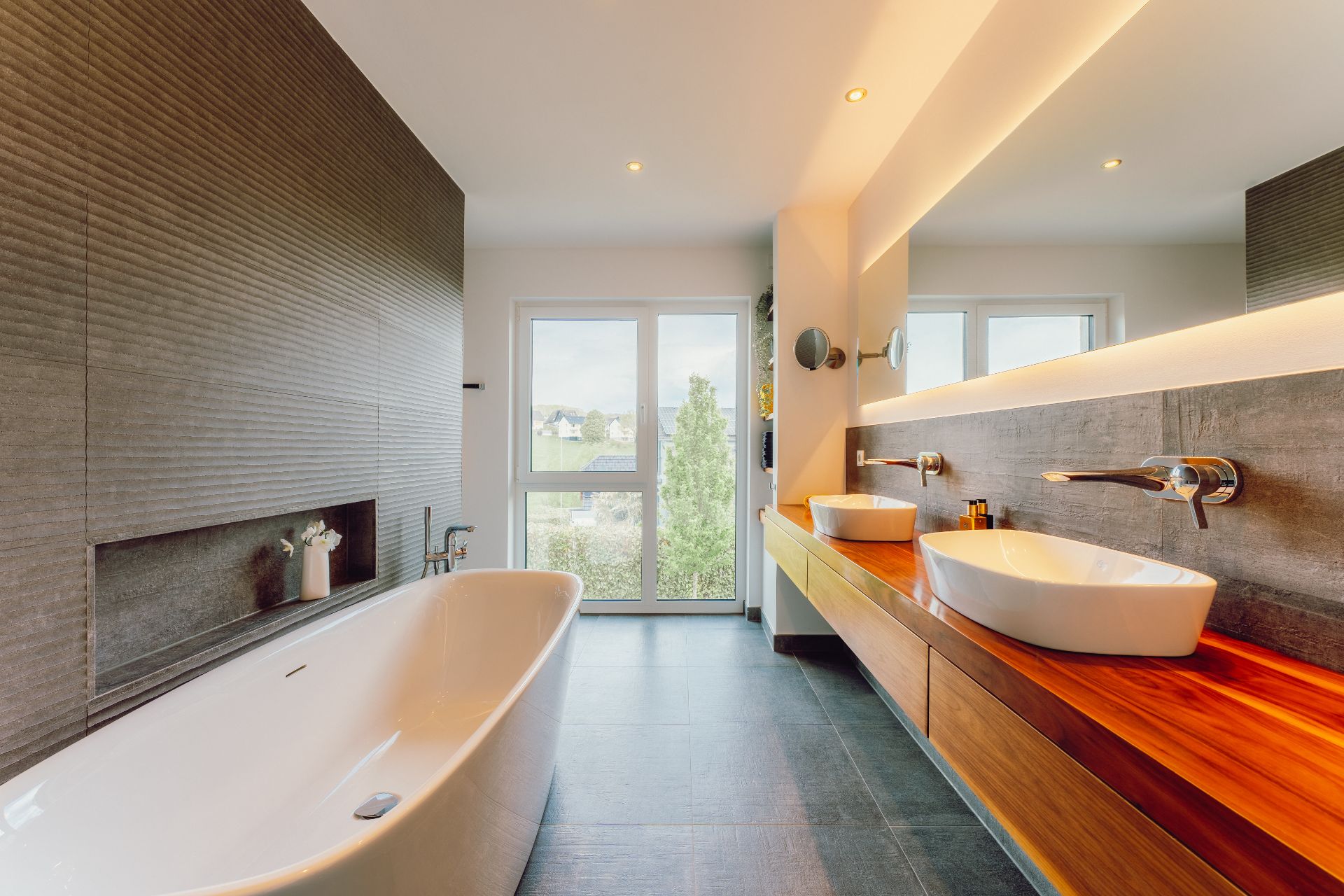 Modernes Badezimmer mit freistehender Badewanne, zwei Waschbecken und großem Fenster.
