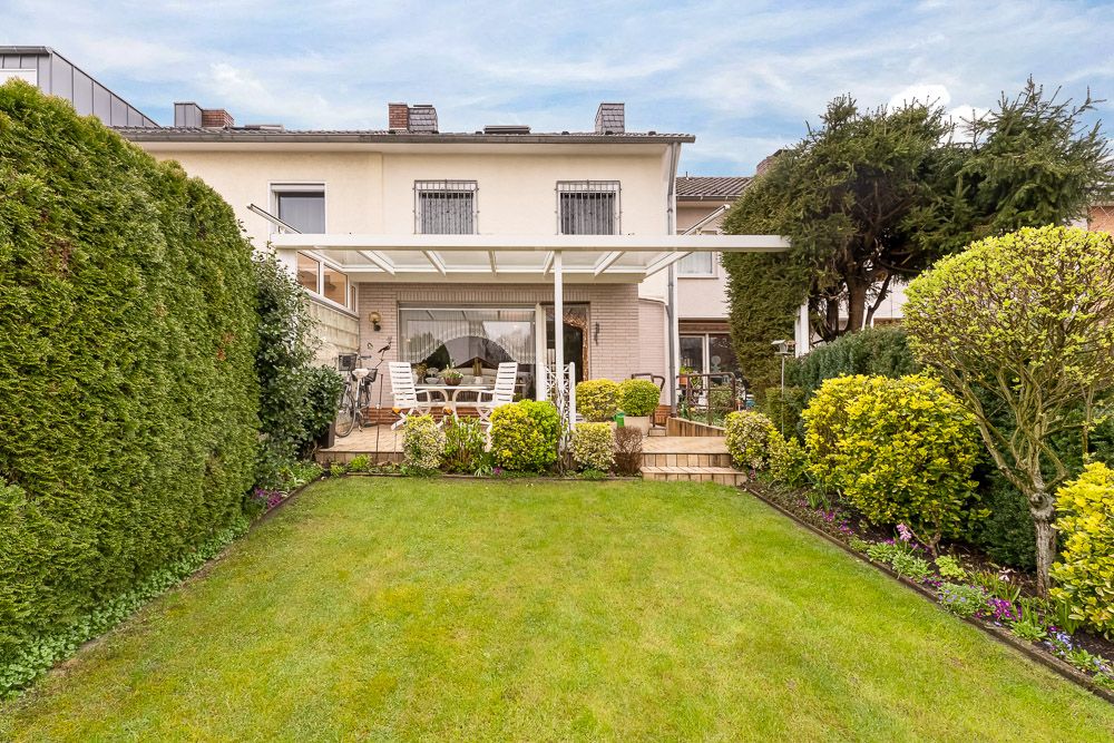 Reihenhaus mit überdachter Terrasse, Garten und Gartenmöbeln, umgeben von Hecken und Büschen.