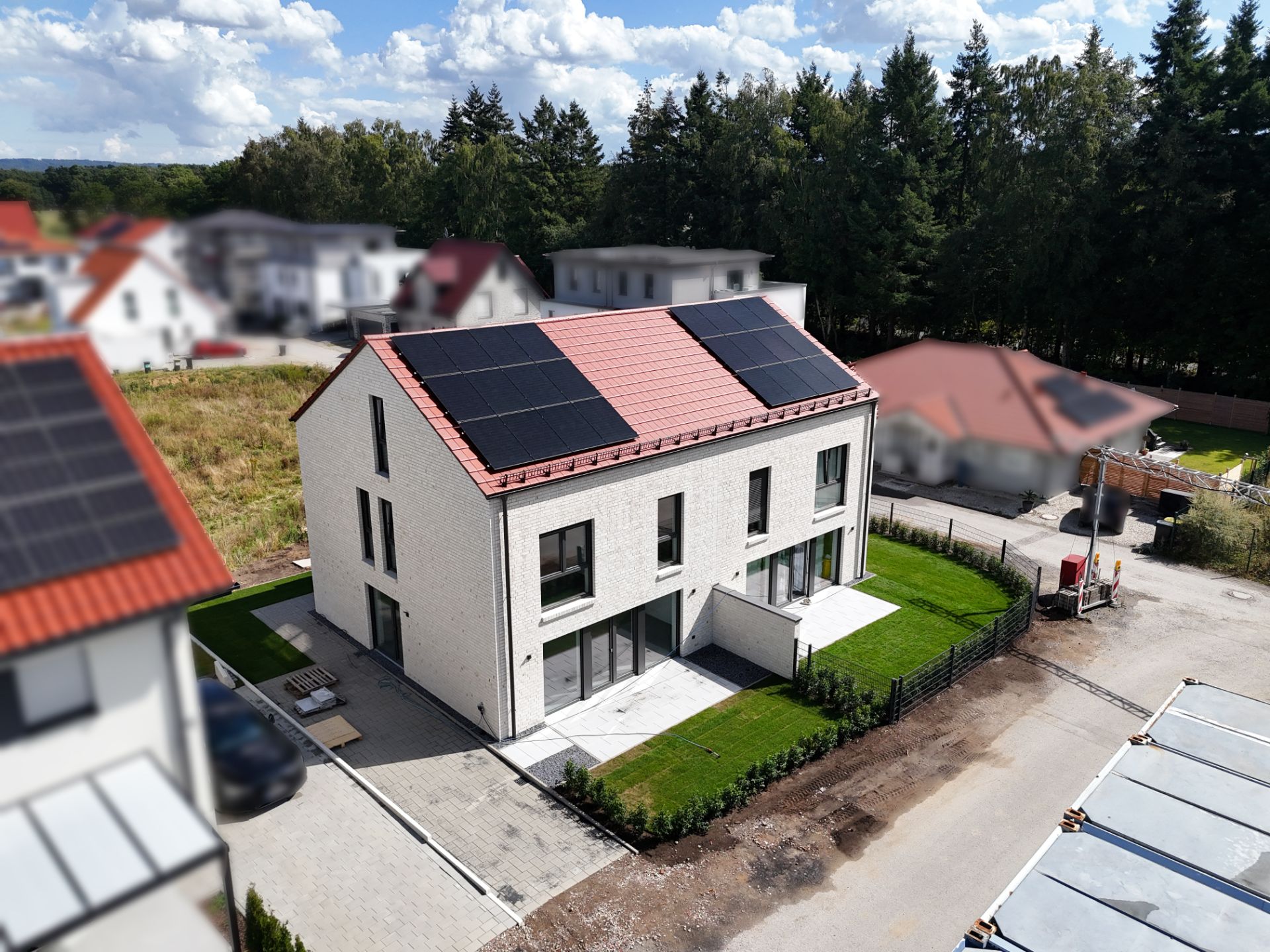Modernes weißes Wohnhaus mit Solarpanels auf dem Dach und kleinem Garten.