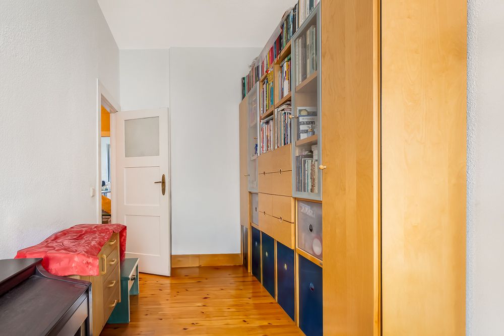 Schmaler Flur mit Bücherregal und Schränken aus Holz, Tür im Hintergrund ist offen.