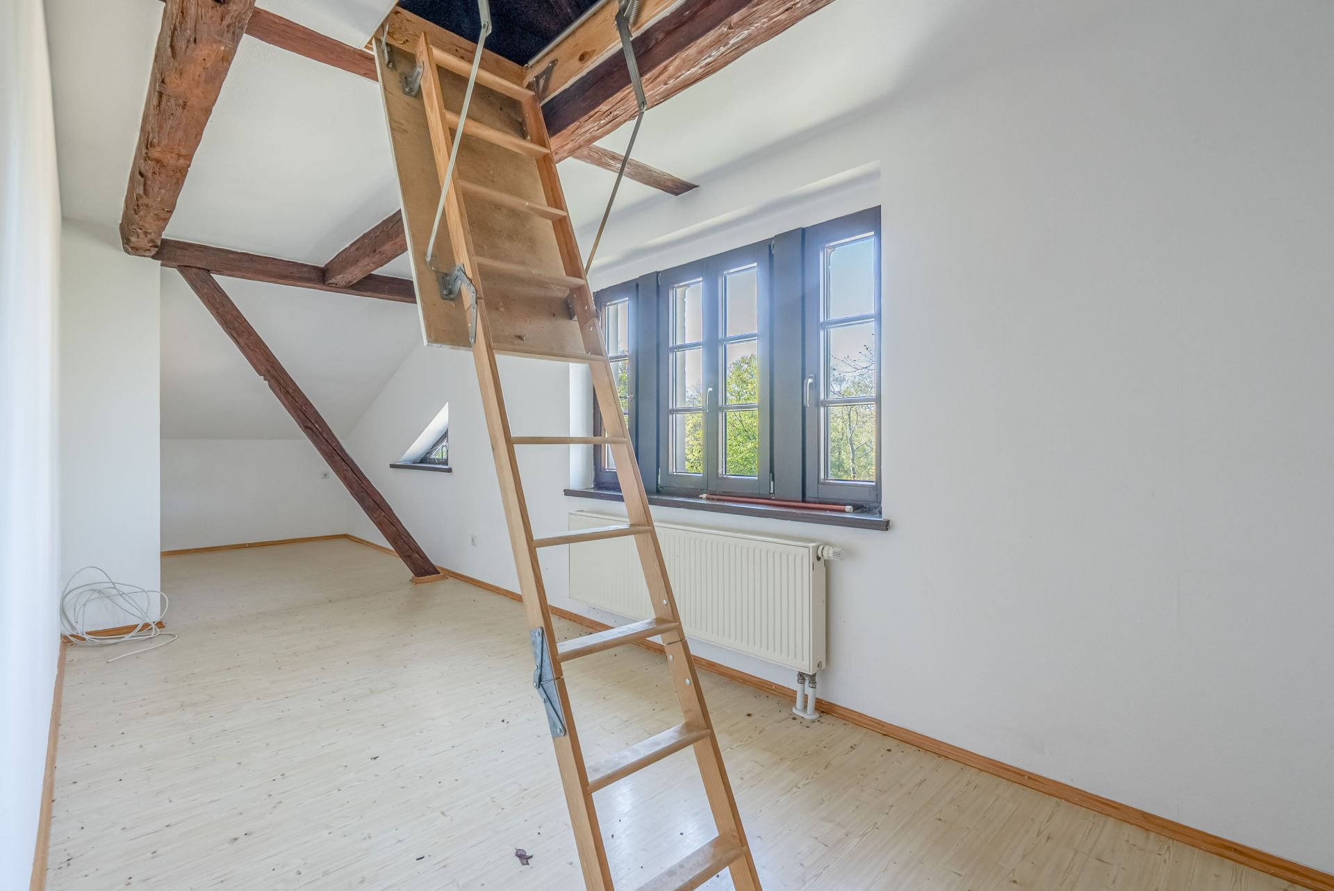 Heller Dachraum mit sichtbaren Holzbalken und einer ausziehbaren Dachbodentreppe.