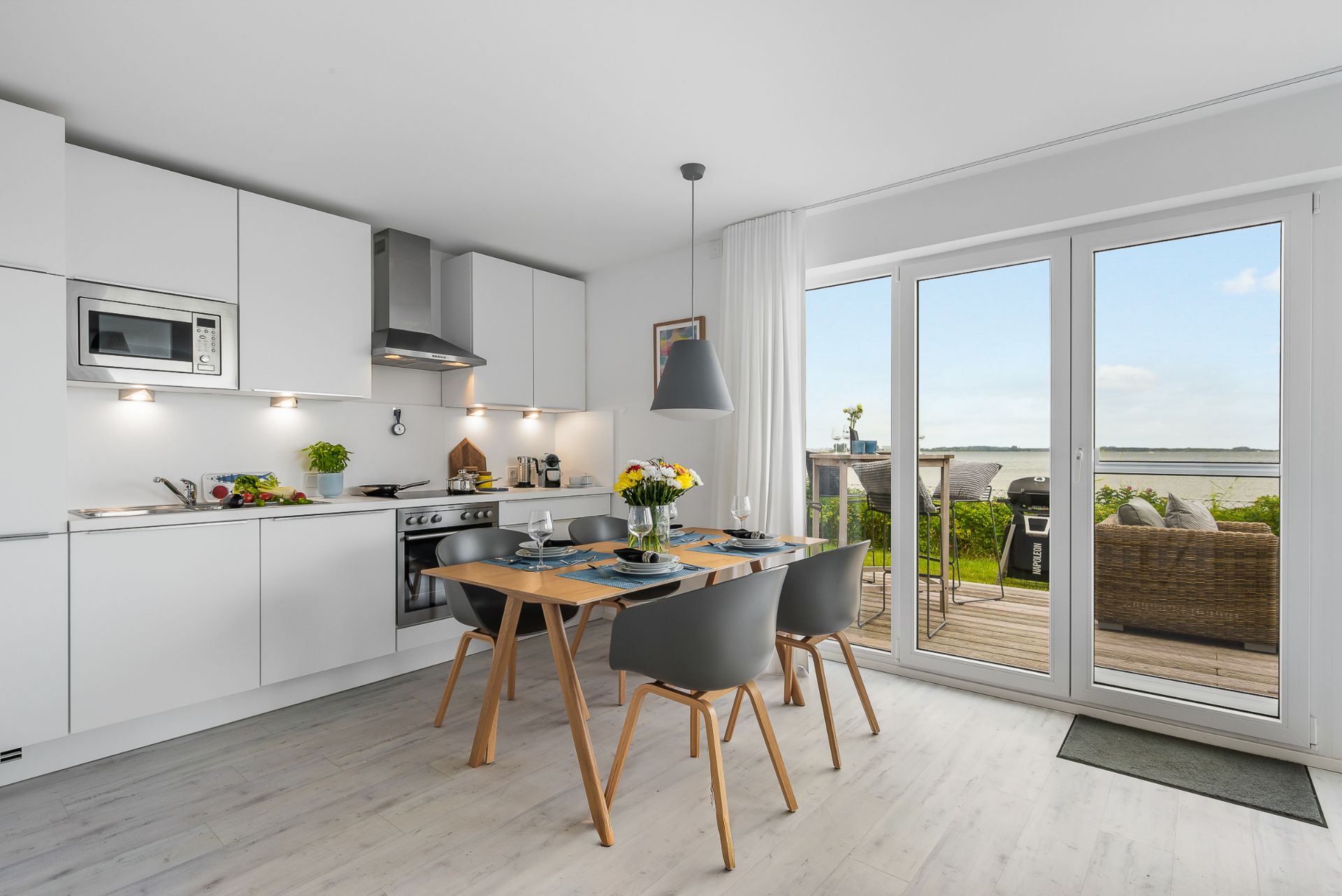 Moderne weiße Küche mit Esstisch und vier Stühlen, große Fenster mit Blick auf Terrasse und Garten.