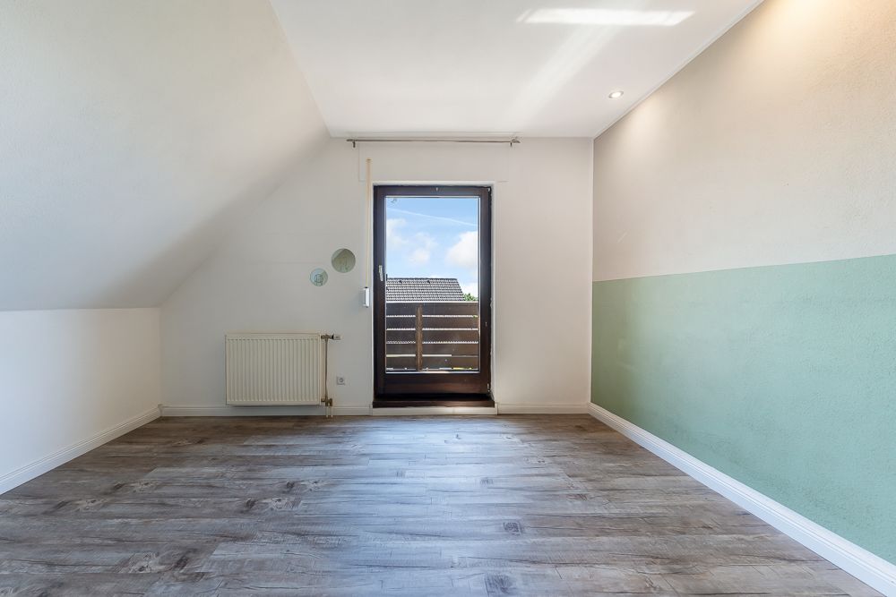 Helles Zimmer mit Holzboden, Heizung, tür zum Balkon und teils grün gestrichener Wand.
