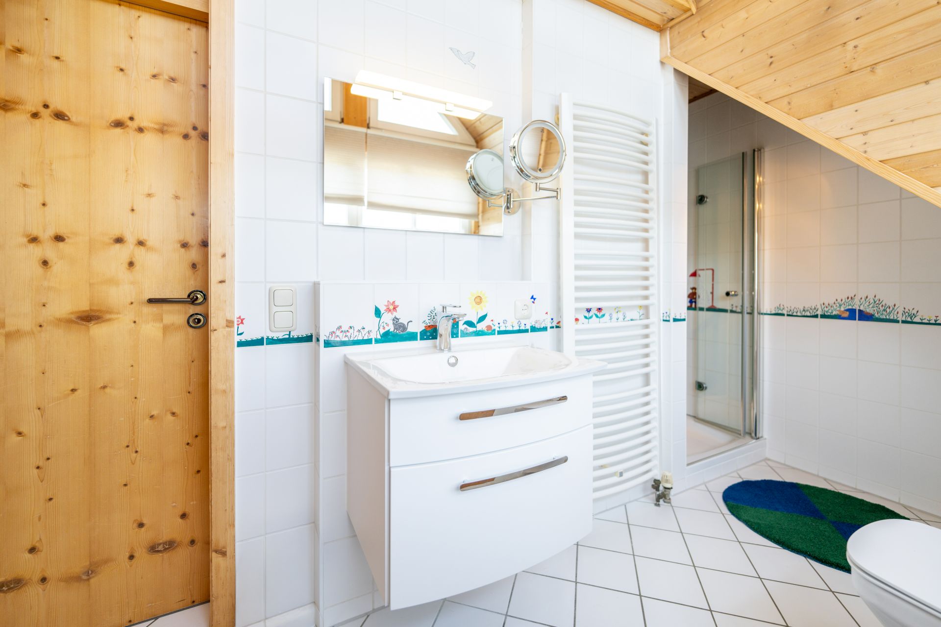 Helles Badezimmer mit Holzdecke, Waschbecken, Spiegel, Dusche und Holz­tür.