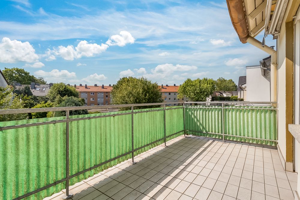 Großer Balkon mit grünem Sichtschutz und Blick auf Bäume und Wohnhäuser.