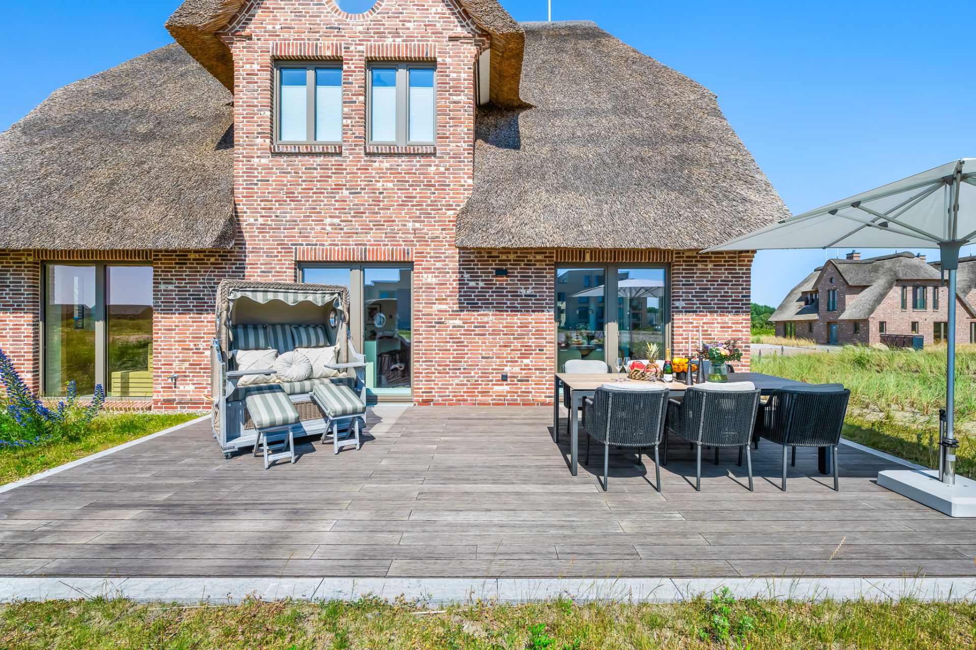 Backsteinhaus mit Reetdach, Terrasse mit Sitzgruppe, Strandkorb und Sonnenschirm.