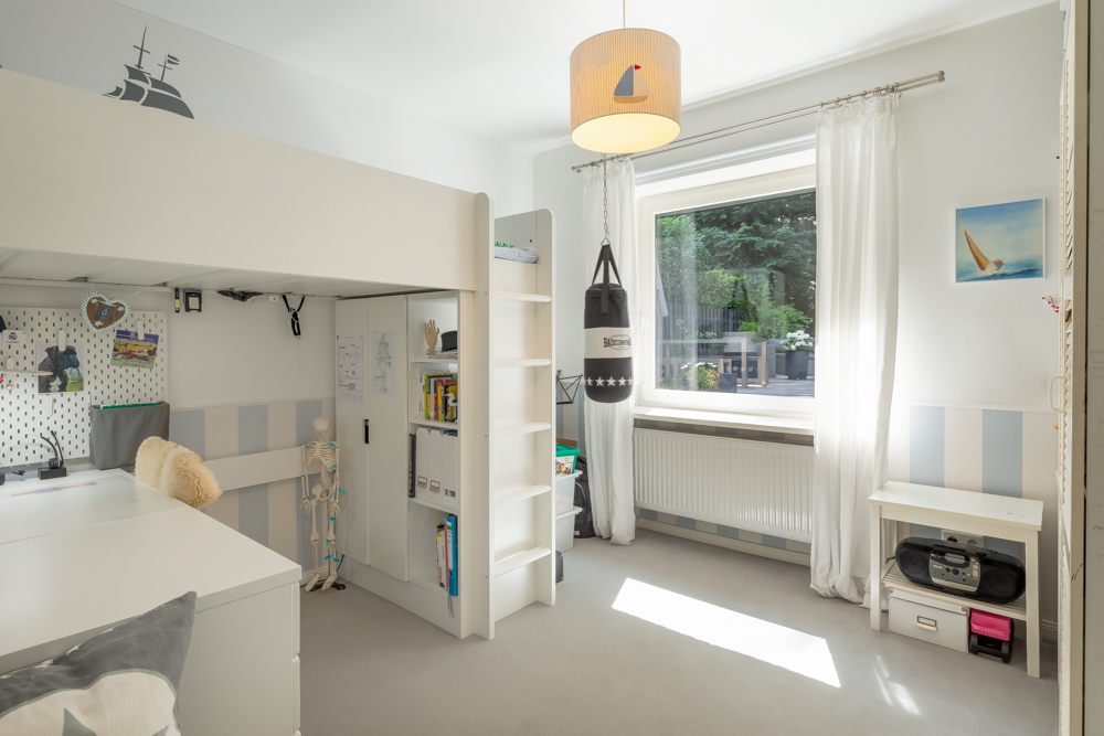 Helles Kinderzimmer mit Hochbett, Schreibtisch, Boxsack und großem Fenster mit Blick in den Garten.