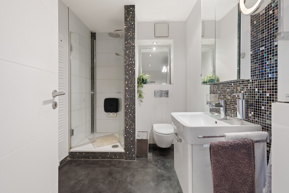 Modernes Badezimmer mit großer Dusche, Wandtoilette, Waschbecken und Spiegel.