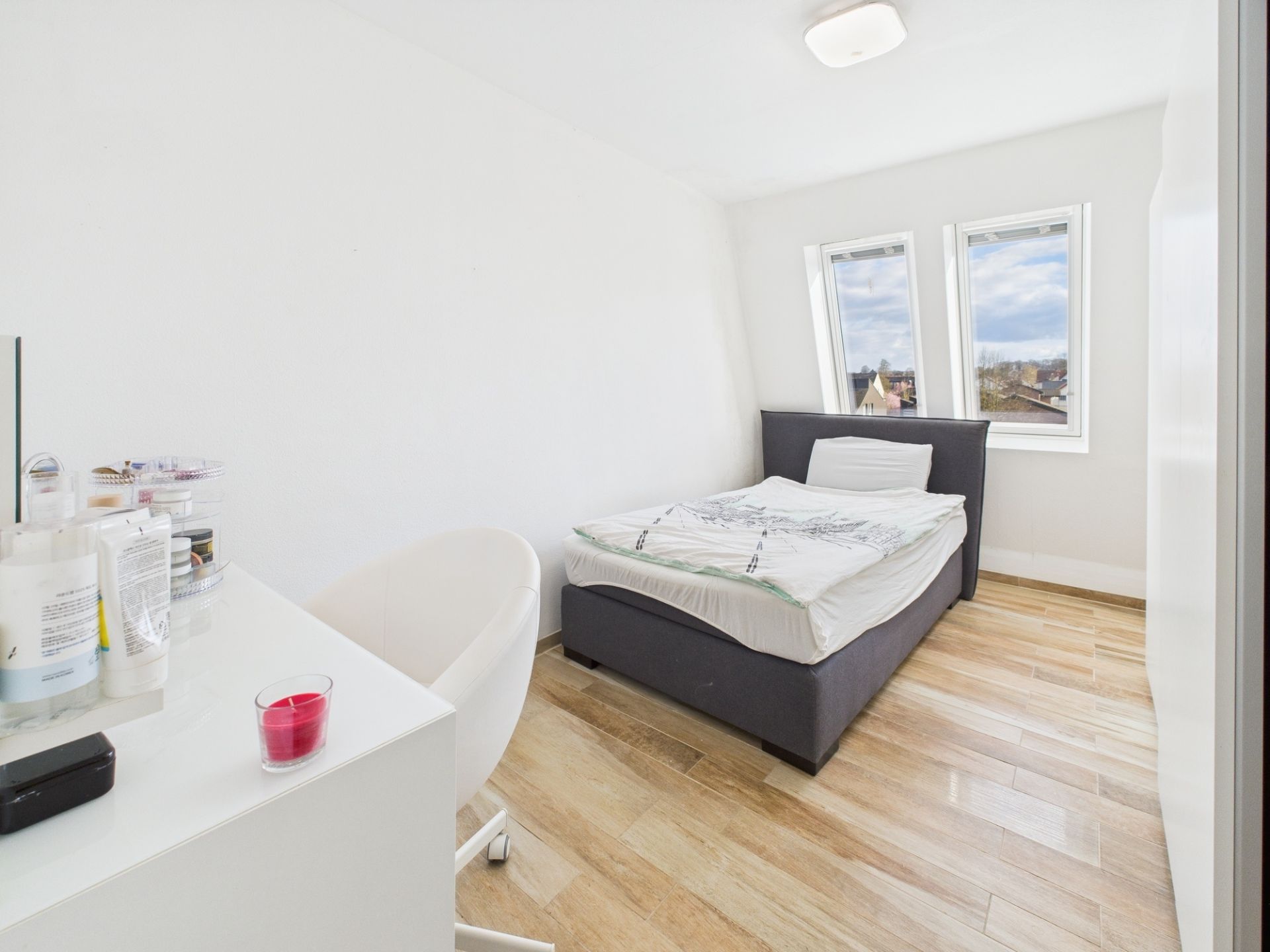 Modernes Schlafzimmer mit Einzelbett, Schreibtisch und zwei Fenstern, helle Holzböden.