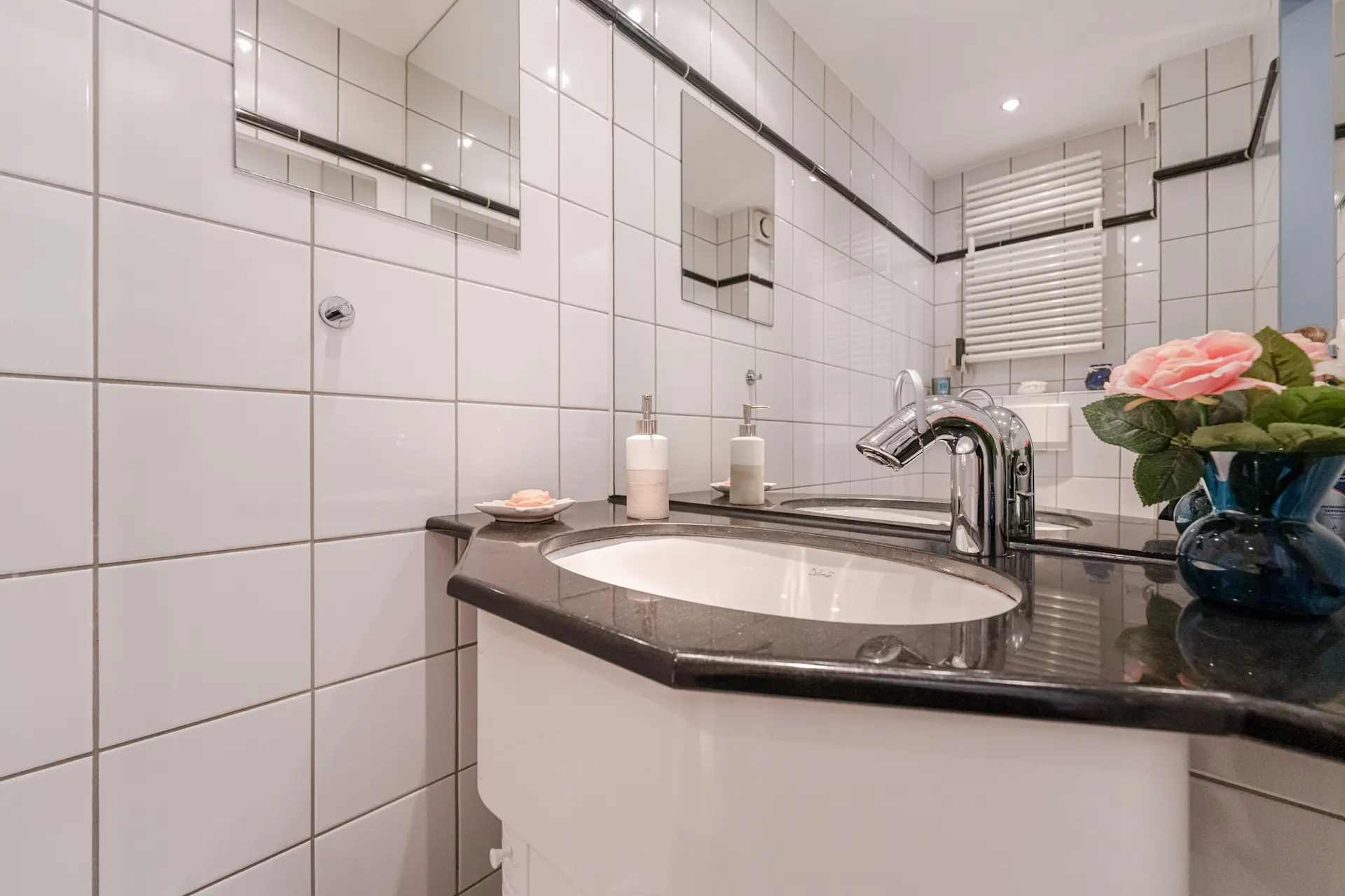 Modernes Badezimmer mit Waschbecken, Spiegel und Vase mit rosa Blumen auf der Ablage.